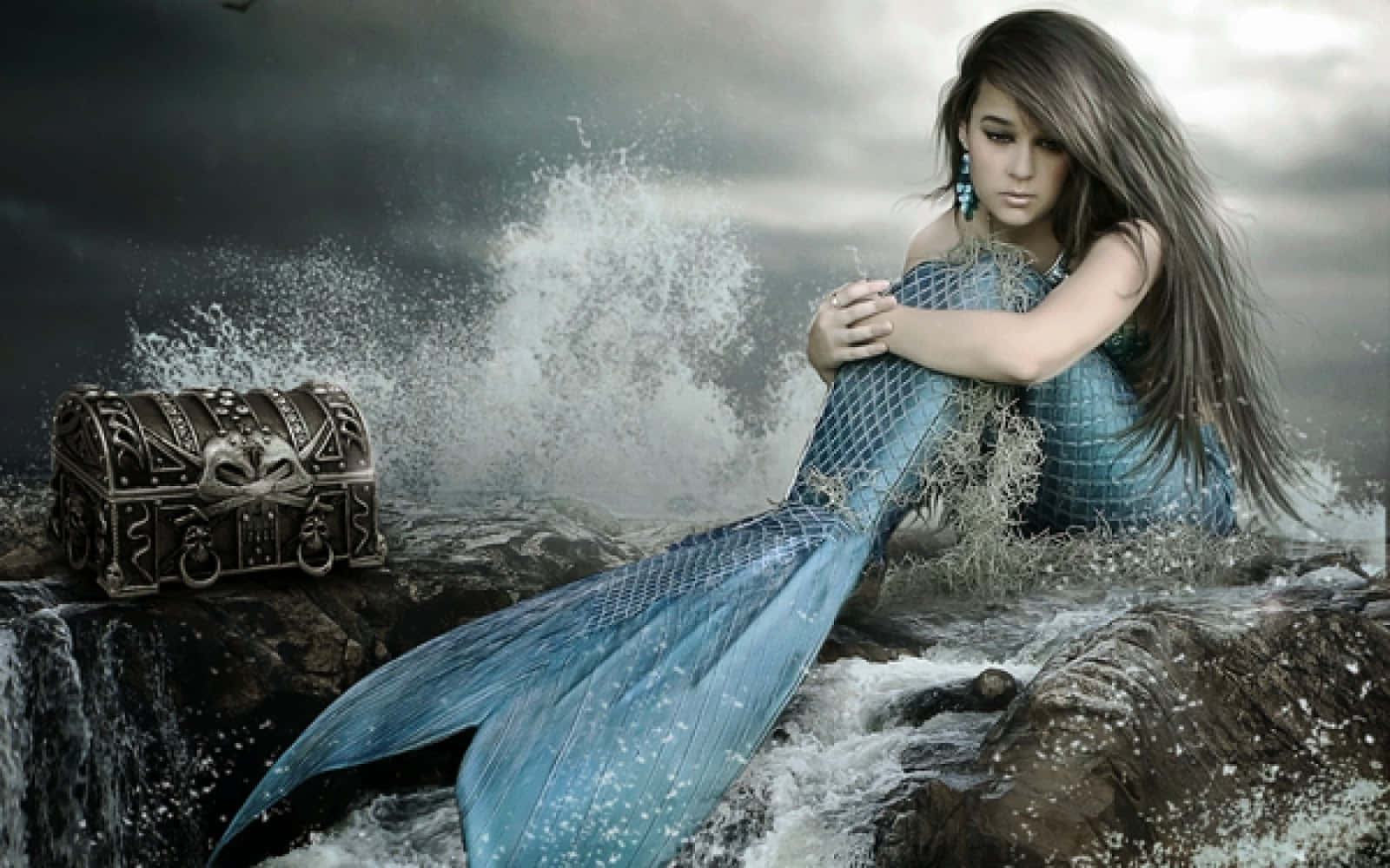 Real Mermaid 桌布 壁紙 — 一條悲傷的美人魚，擁有藍色鱗片的尾巴，坐在風暴中的岩石上，旁邊有一個華麗的寶箱，海浪在她周圍拍打。