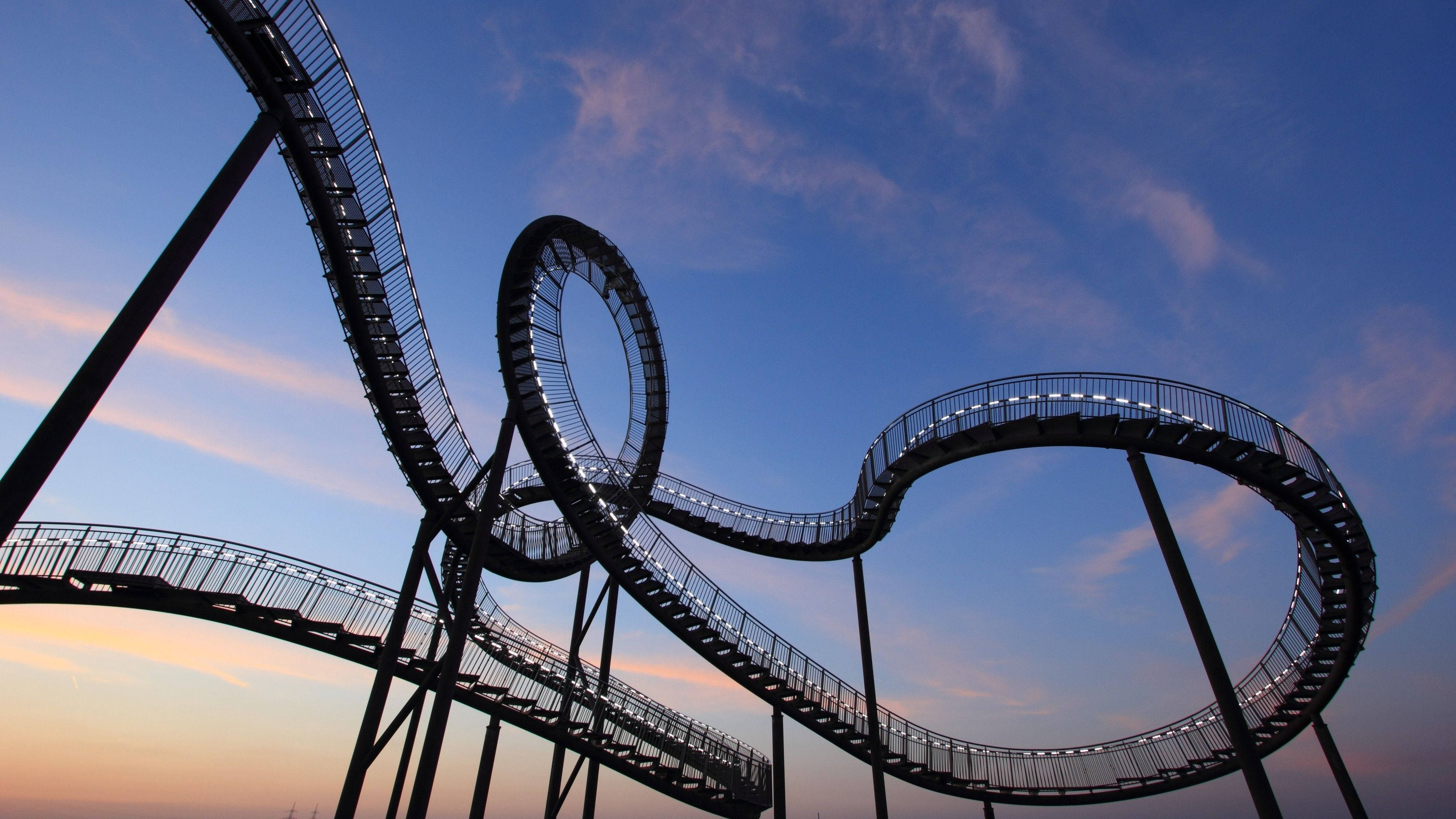 Roller Coaster 桌布 壁紙 — 一條扭曲的照明空中步道在帶有柔和粉紅色和藍色色調的暮色天空中盤旋。