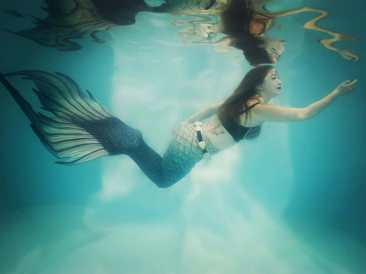 Real Mermaid 桌布 壁紙 — 一條擁有精細鱗片尾巴的美人魚在清澈的碧綠海水中優雅地滑行，光線從上方穿透水面。