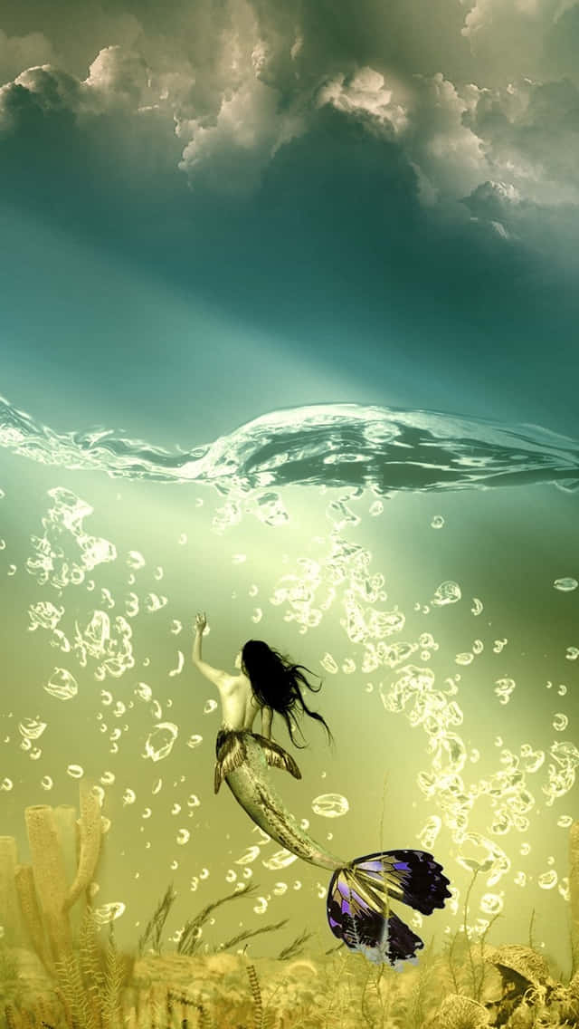 美人魚 桌布 壁紙 — 一條擁有蝴蝶尾鰭的美人魚，穿過陽光照射的水域，向著多雲的天空游去，周圍環繞著氣泡和海草。