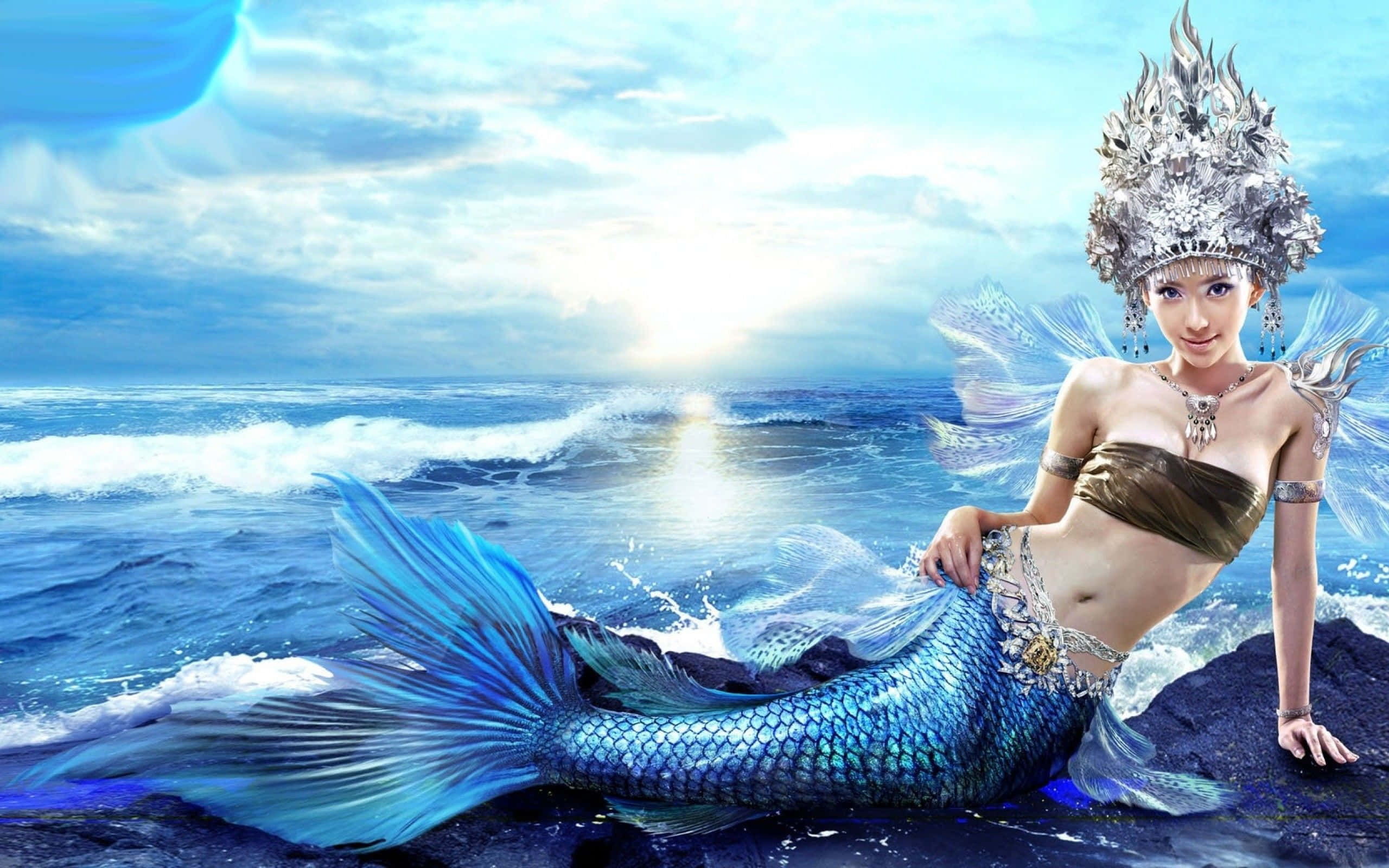美人魚 桌布 壁紙 — 一條擁有閃爍藍色尾巴和華麗銀冠的美人魚優雅地坐在海洋岩石上，陽光在她身後的海浪上閃爍。