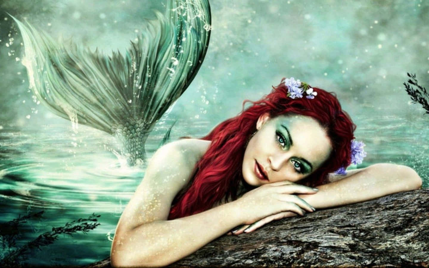 Mermaids 桌布 壁紙 — 一條擁有鮮豔紅髮和綠色尾巴的美人魚，在藍綠色水中將下巴擱在木頭上，並以紫色花朵裝飾。