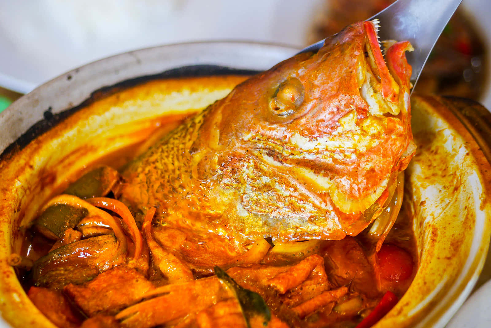 Food Photography 桌布 壁紙 — 一條整魚從一個裝有豐富橙色咖哩的陶鍋中撈起的特寫，可見香料和蔬菜。