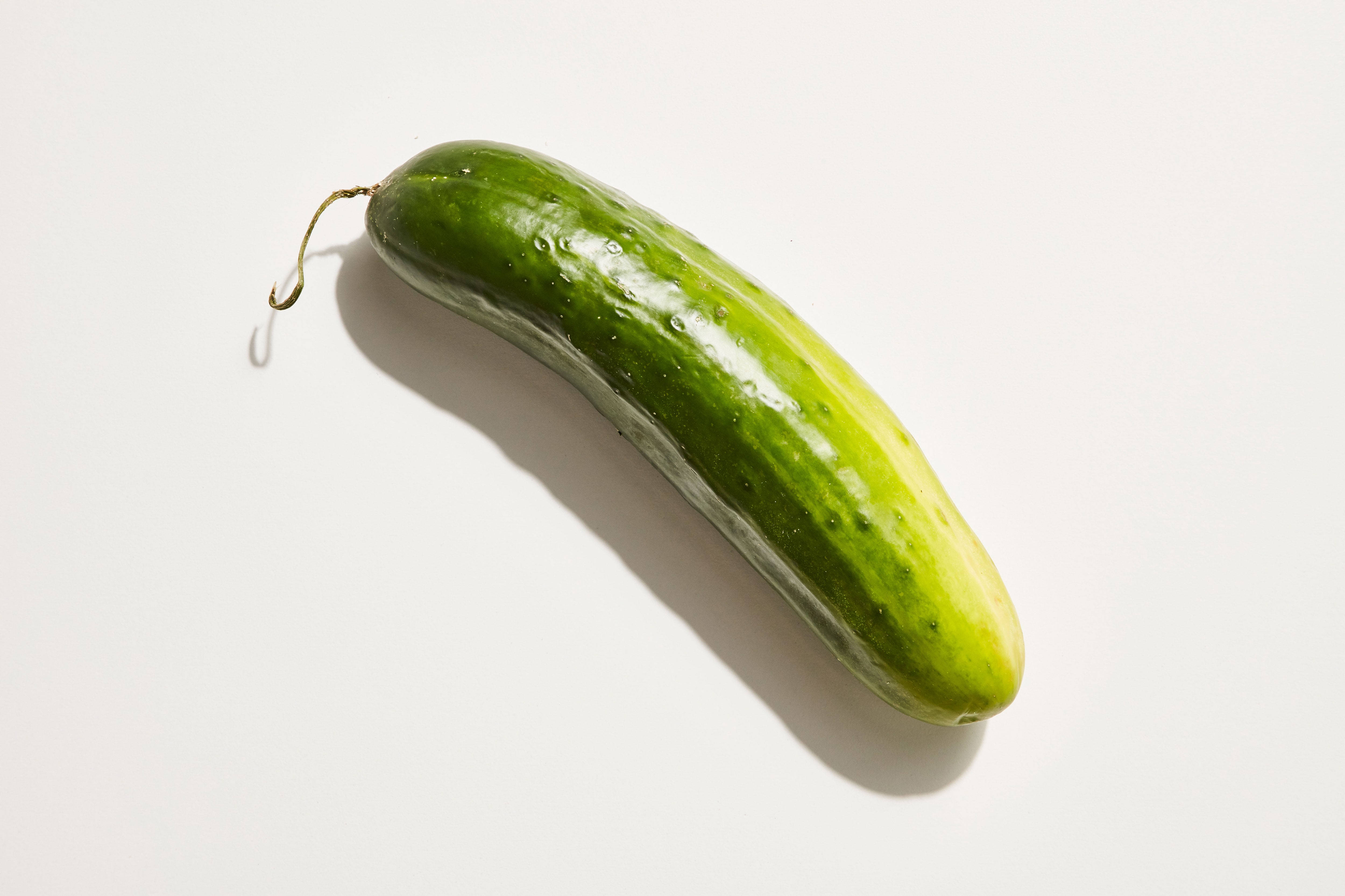 Fruit 桌布 壁紙 — 一條新鮮的綠色小黃瓜帶有水珠，斜放在純白色表面上，投下柔和陰影。