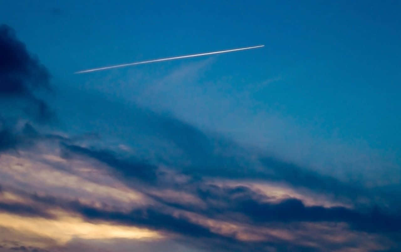 comet 桌布 壁紙 — 一條明亮的飛機雲劃過塗滿深藍色和金色雲彩的暮色天空。