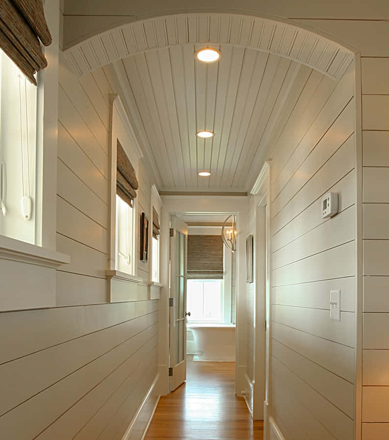 Shiplap 桌布 壁紙 — 一條明亮通風的走廊，配有白色護牆板牆壁和天花板拱門，通往陽光充足的浴室。
