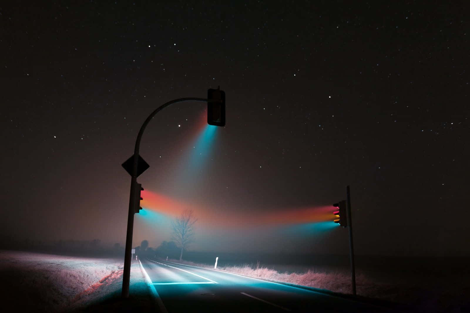 Stop Light 桌布 壁紙 — 一條星光燦爛的夜路，被發光的交通燈照亮，透過霧氣投射出色彩繽紛的光束。