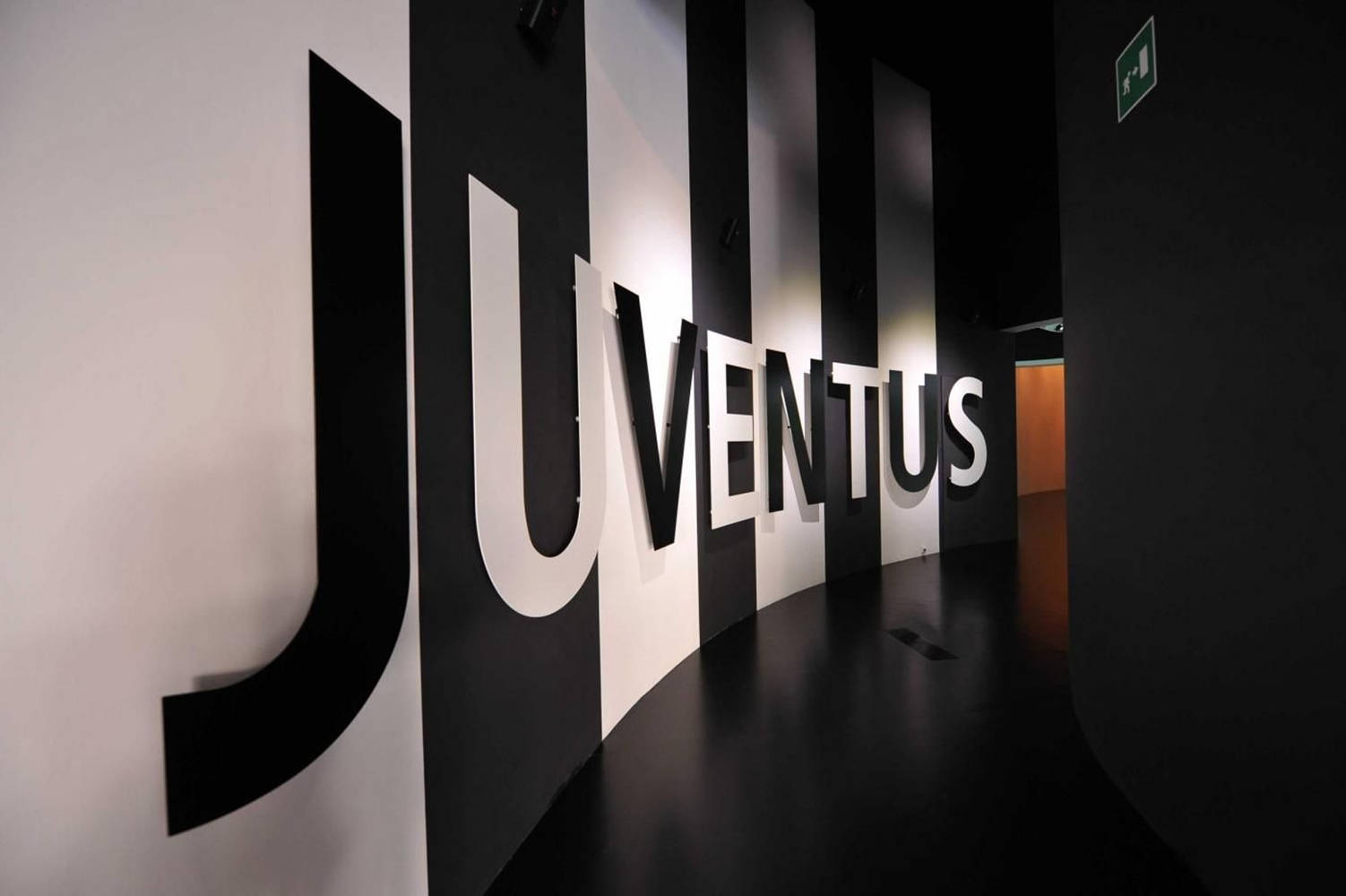 足球 桌布 壁紙 — 一條時尚的黑白走廊，設有巨大的發光「JUVENTUS」字母，在光亮的地板上投射出戲劇性的陰影。