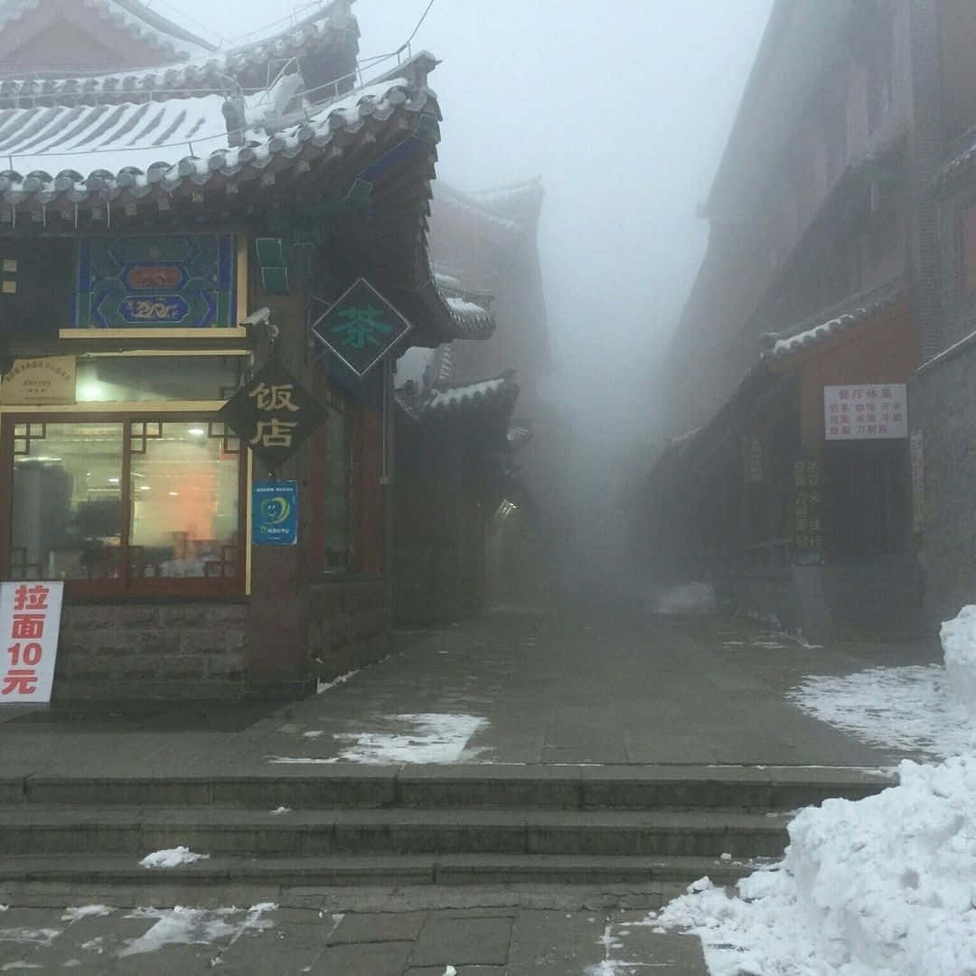 灰色美學動圖 桌布 壁紙 — 一條有雪有霧的小巷，位於傳統中國小鎮，屋頂覆蓋白雪，商店招牌閃爍發光。