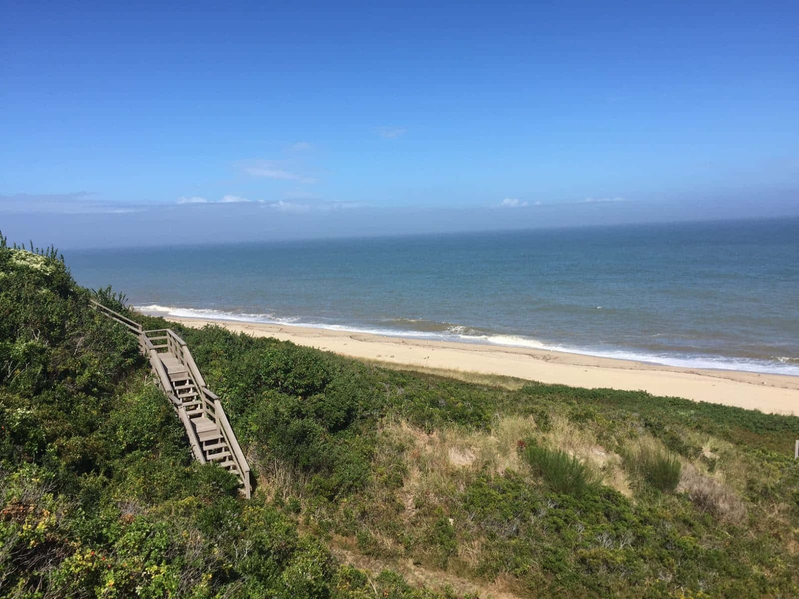 Seaside 桌布 壁紙 — 一條木樓梯蜿蜒而下，穿過鬱鬱蔥蔥的綠色沙丘，通往晴朗藍天下寧靜的沙灘。