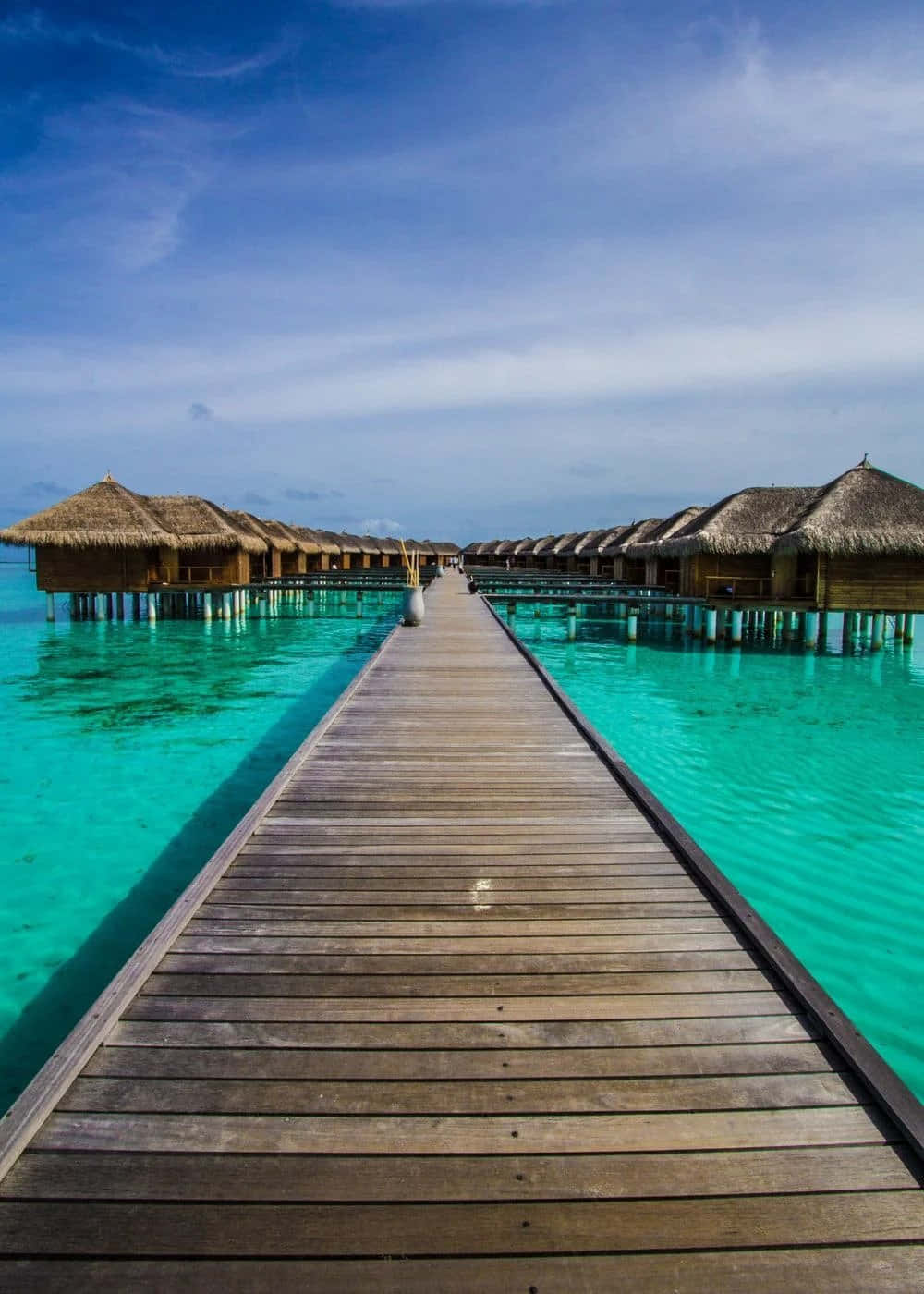 Vacation Mode 桌布 壁紙 — 一條木製碼頭伸向茅草屋頂的水上平房，天空湛藍清澈。