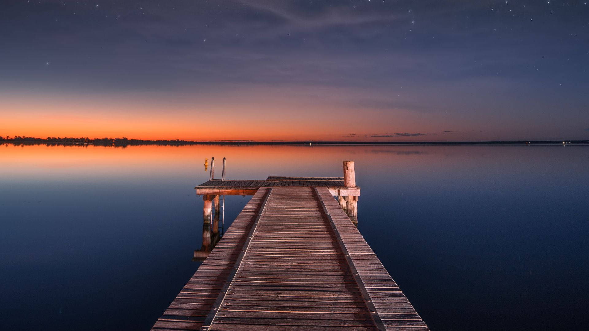 Dock 桌布 壁紙 — 一條木製碼頭延伸到平靜的湖面上，天空繁星點點，暮色中地平線泛著橙色光芒。