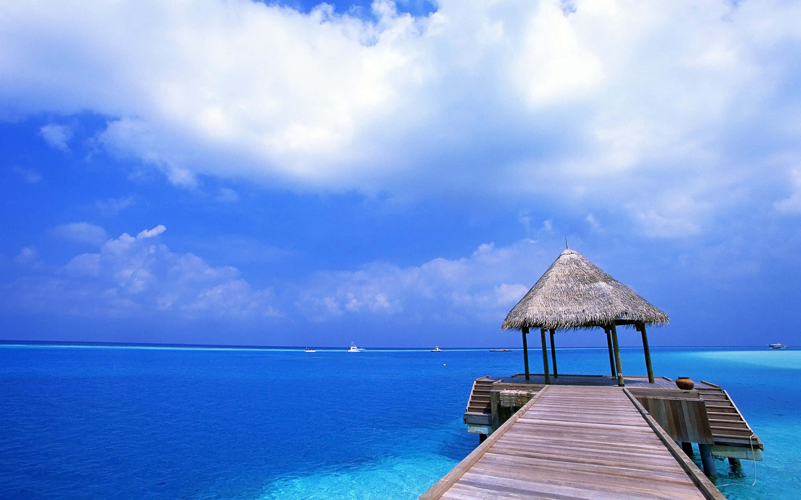 Mexican Beach 桌布 壁紙 — 一條木製碼頭延伸至充滿活力的碧綠海水，通往一個茅草屋頂的涼亭，上方是晴朗的藍天和蓬鬆的白雲。