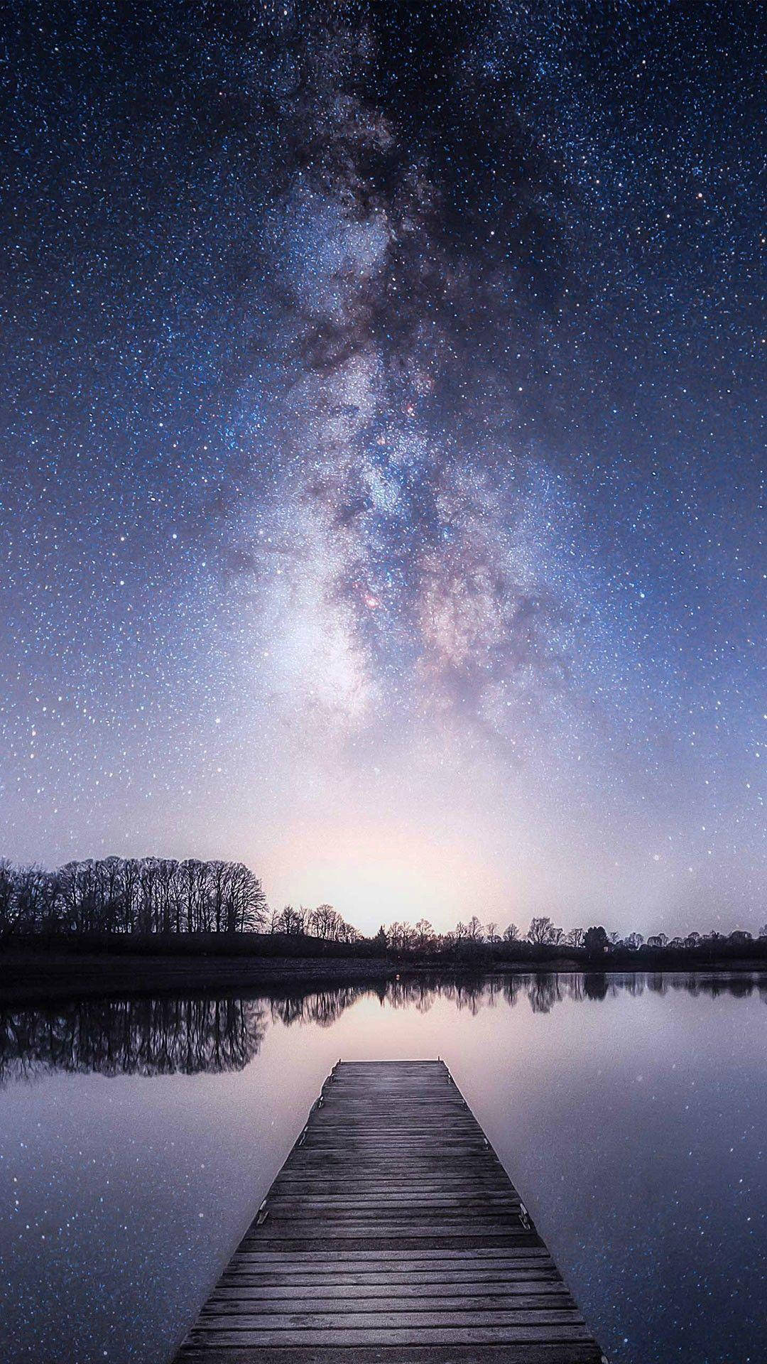 Xiaomi 桌布 壁紙 — 一條木製碼頭延伸至平靜的湖面，上方是壯麗的星空，銀河拱橋般橫跨天際。
