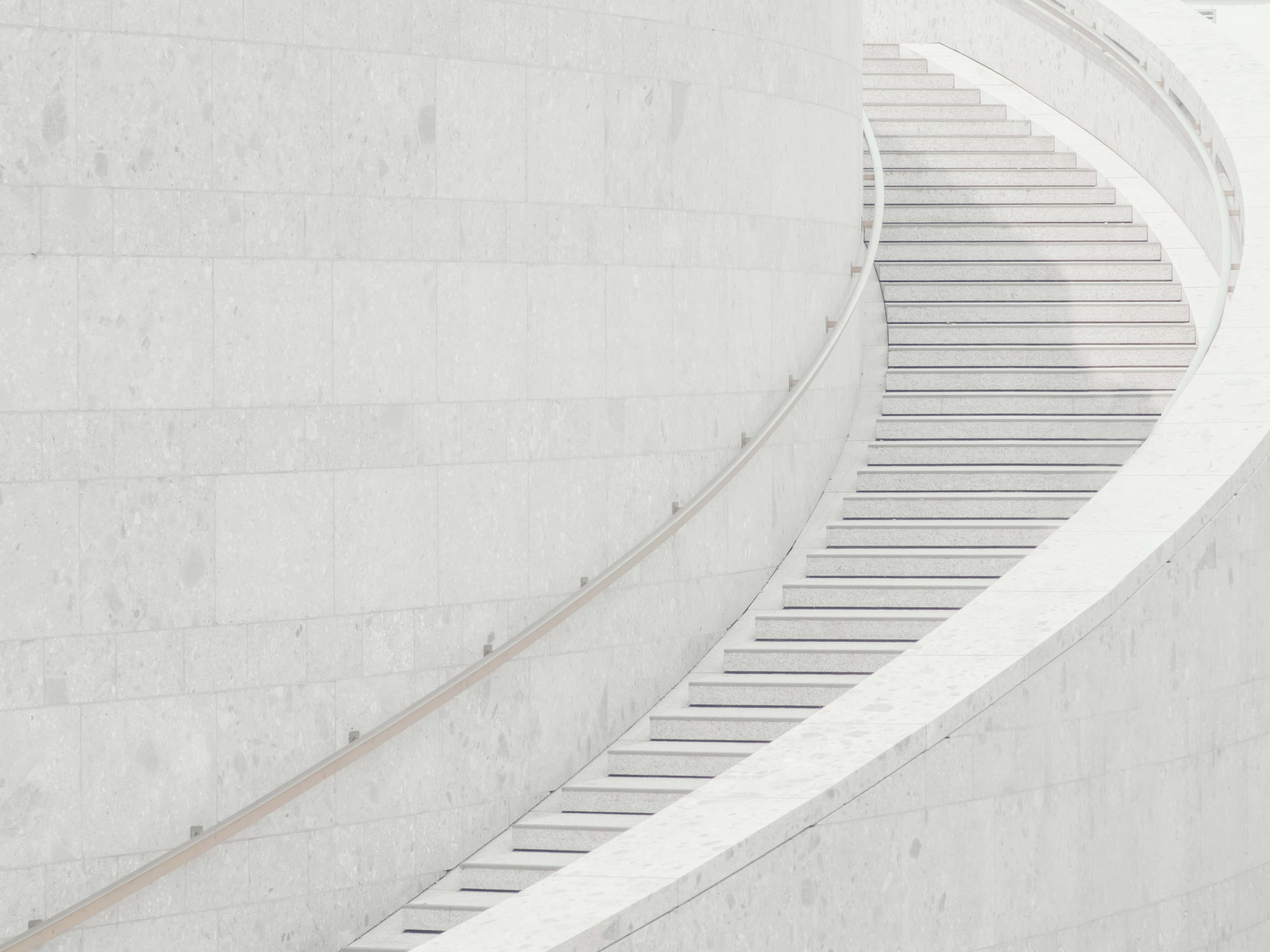 Steps 桌布 壁紙 — 一條極簡風格的弧形樓梯，採用光滑白色石材，在柔和日光下沿著相配的牆壁優雅上升。