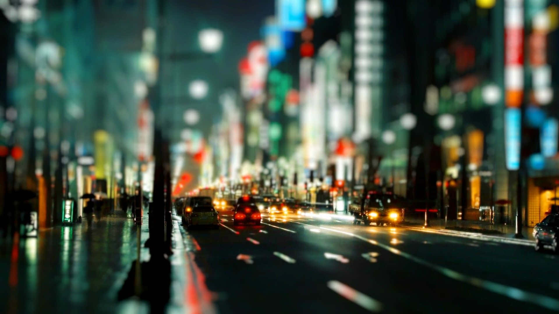 City Lights 桌布 壁紙 — 一條模糊的夜晚城市街道，有發光的霓虹燈和流動的車頭燈反射在濕漉漉的路面上。