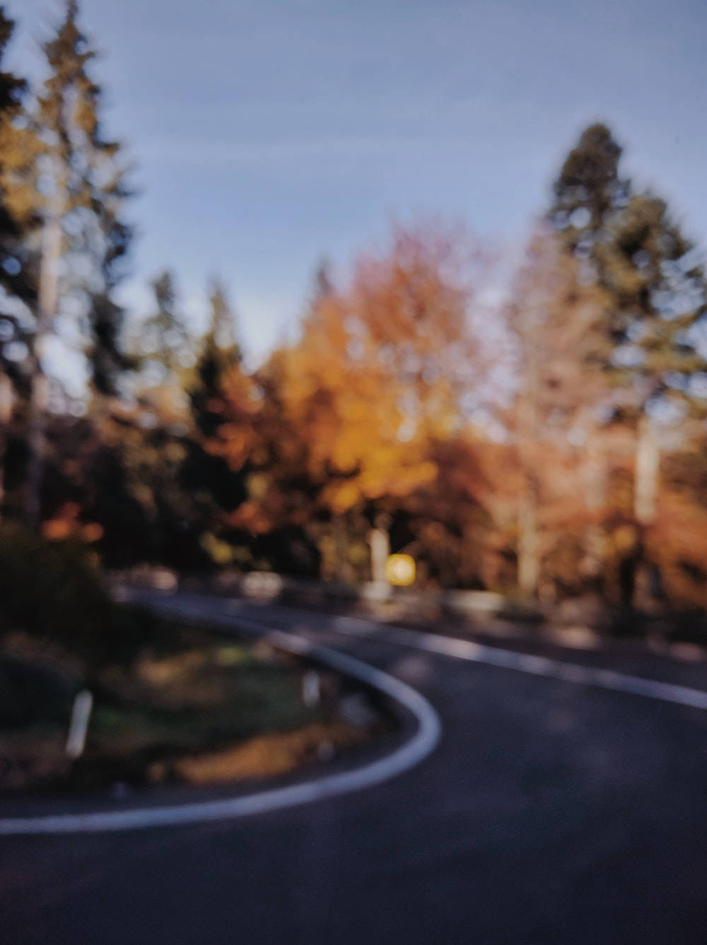 Dslr 桌布 壁紙 — 一條模糊的秋天道路蜿蜒穿過一片金色樹葉的森林，在清澈的藍天下。