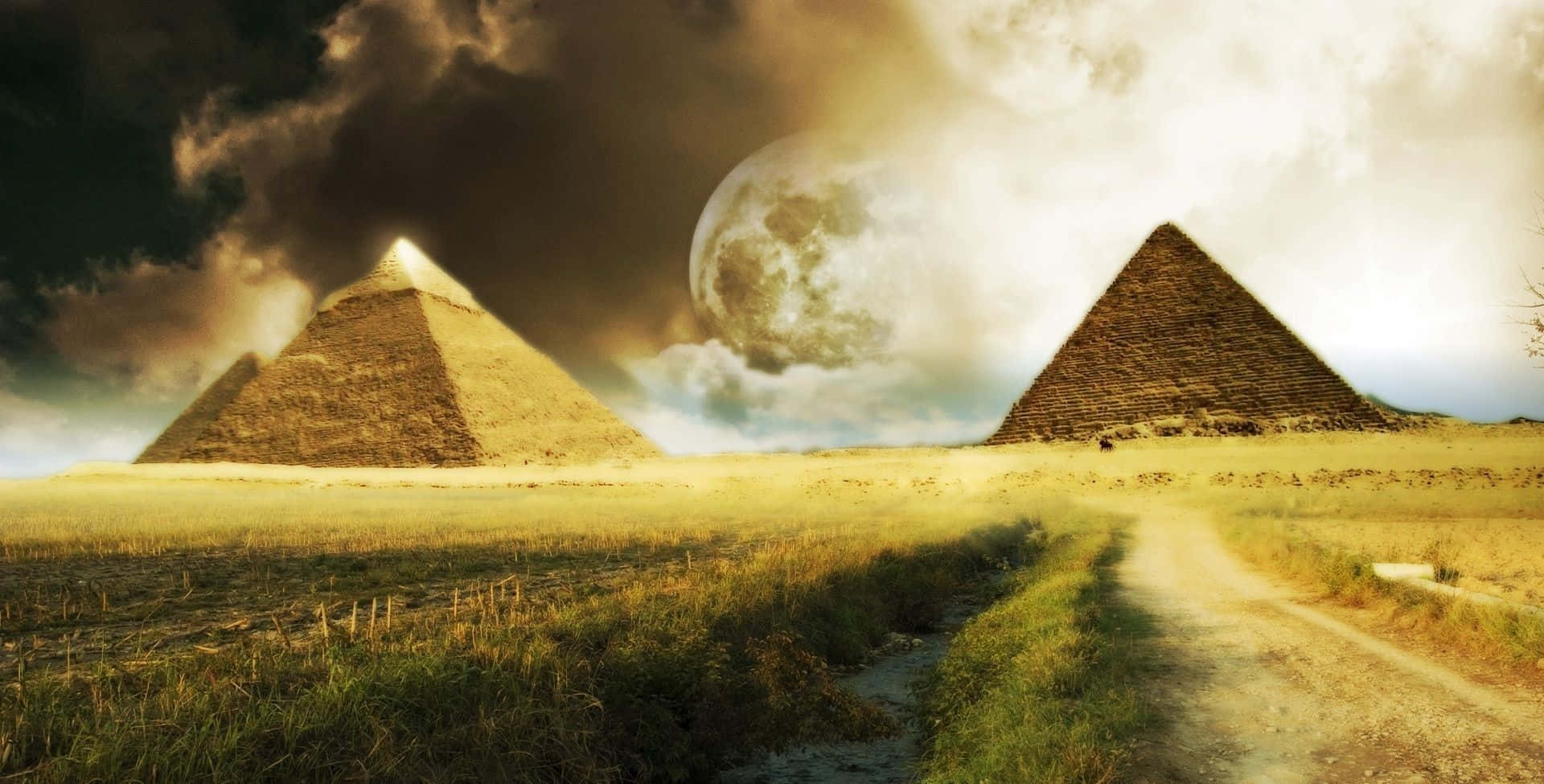 埃及 桌布 壁紙 — 一條泥土路通向兩座古老金字塔，天空戲劇性，有巨大月亮和烏雲。