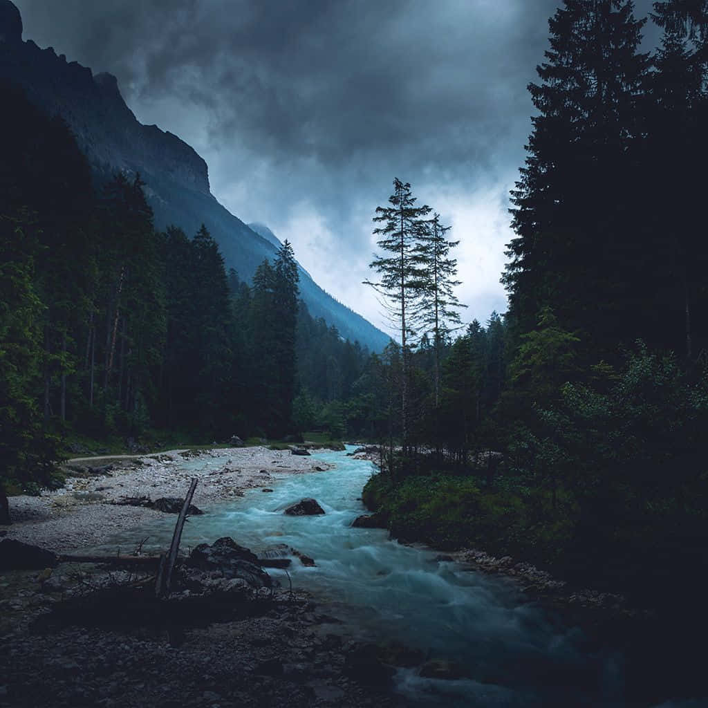 桌布 壁紙 — 一條湍急的河流在暴風雨黃昏的天空下，衝過黑暗的森林山谷。