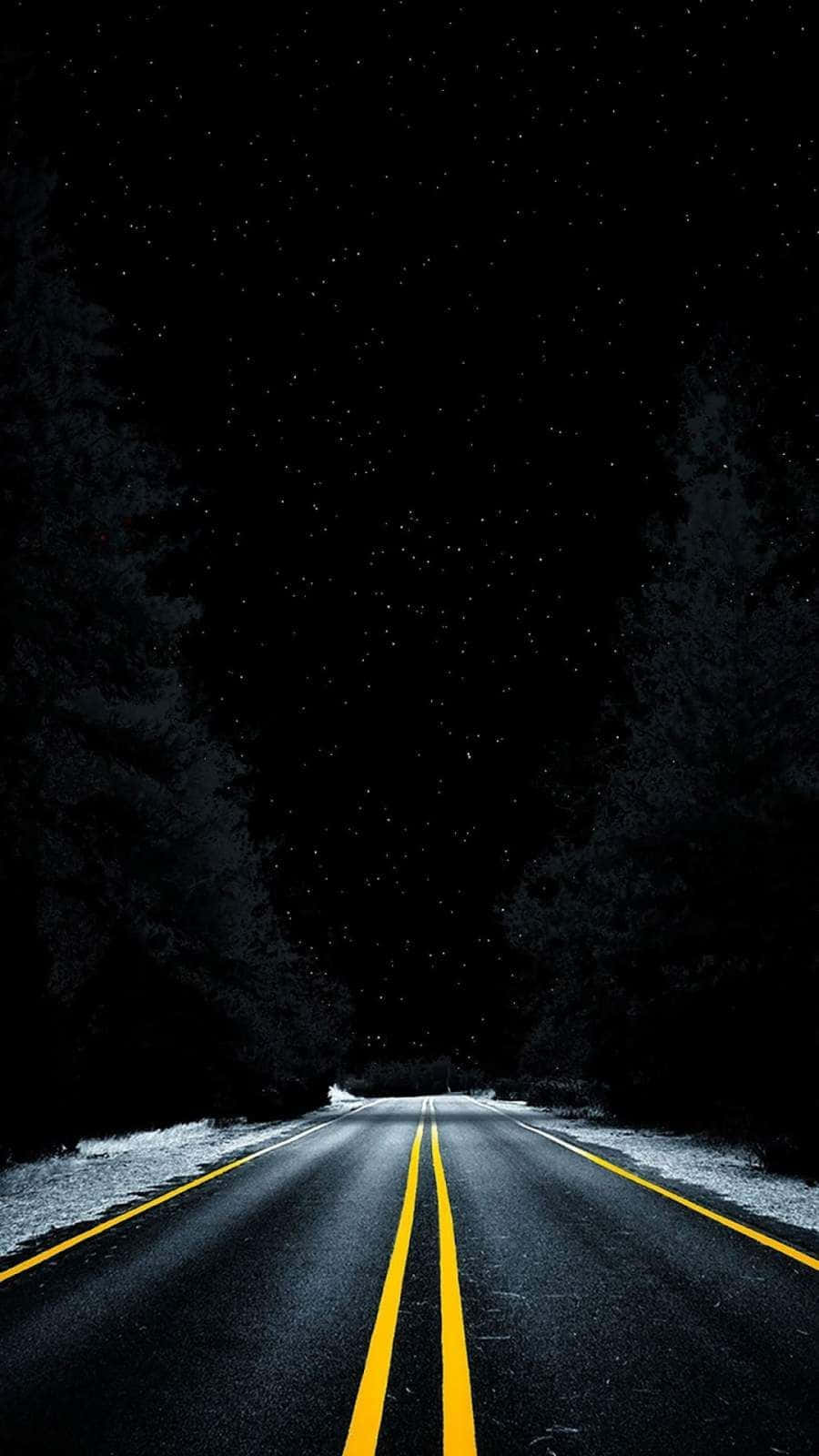 Dark Road 桌布 壁紙 — 一條漆黑的瀝青道路，帶有明亮的黃色線條，在繁星點點的夜空下延伸至遠方，兩旁是覆蓋著白雪的樹木。
