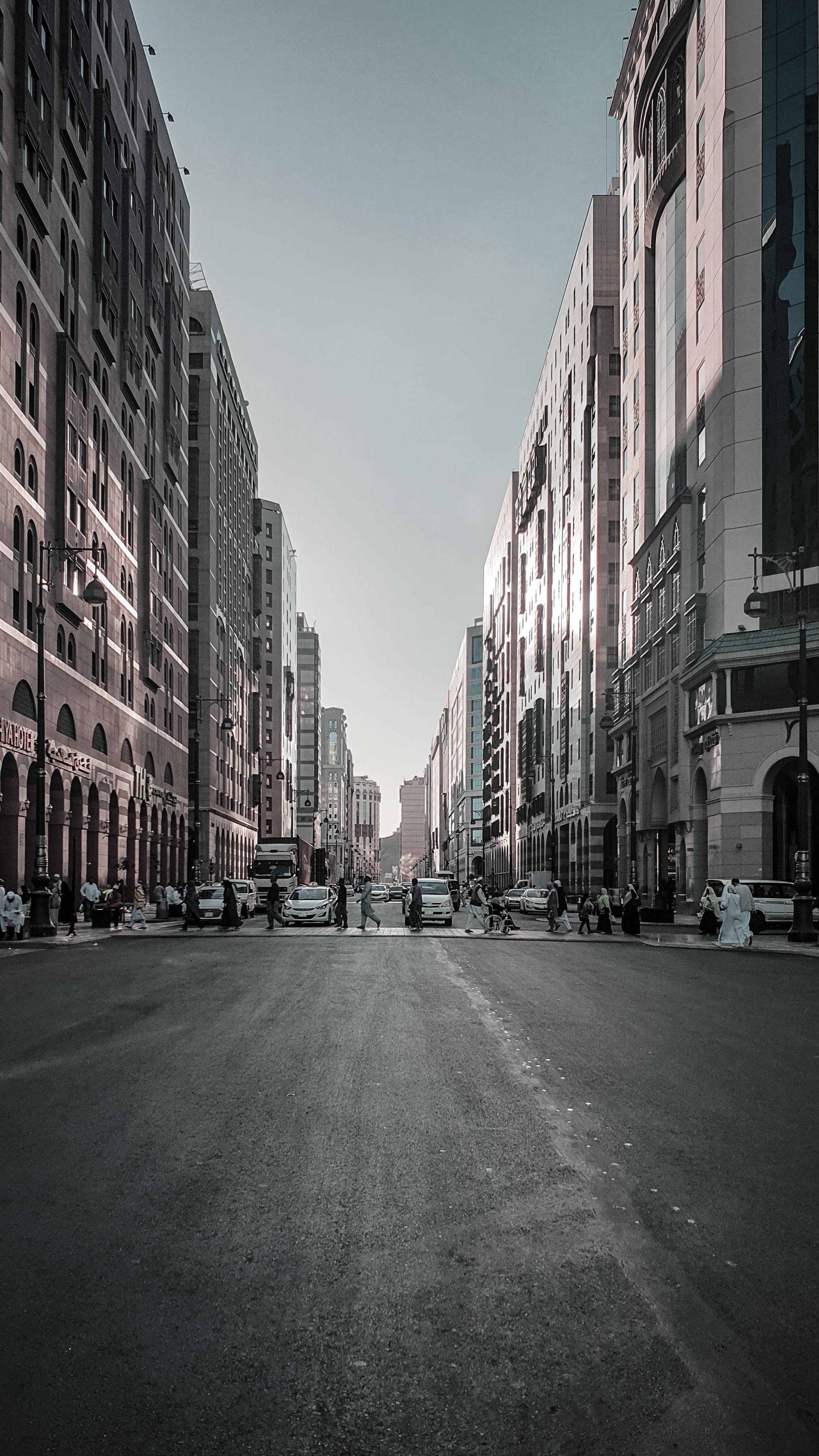 Street 桌布 壁紙 — 一條漫長的城市街道，兩旁是高樓大廈，蒼白的天空下，遠處有行人和汽車。