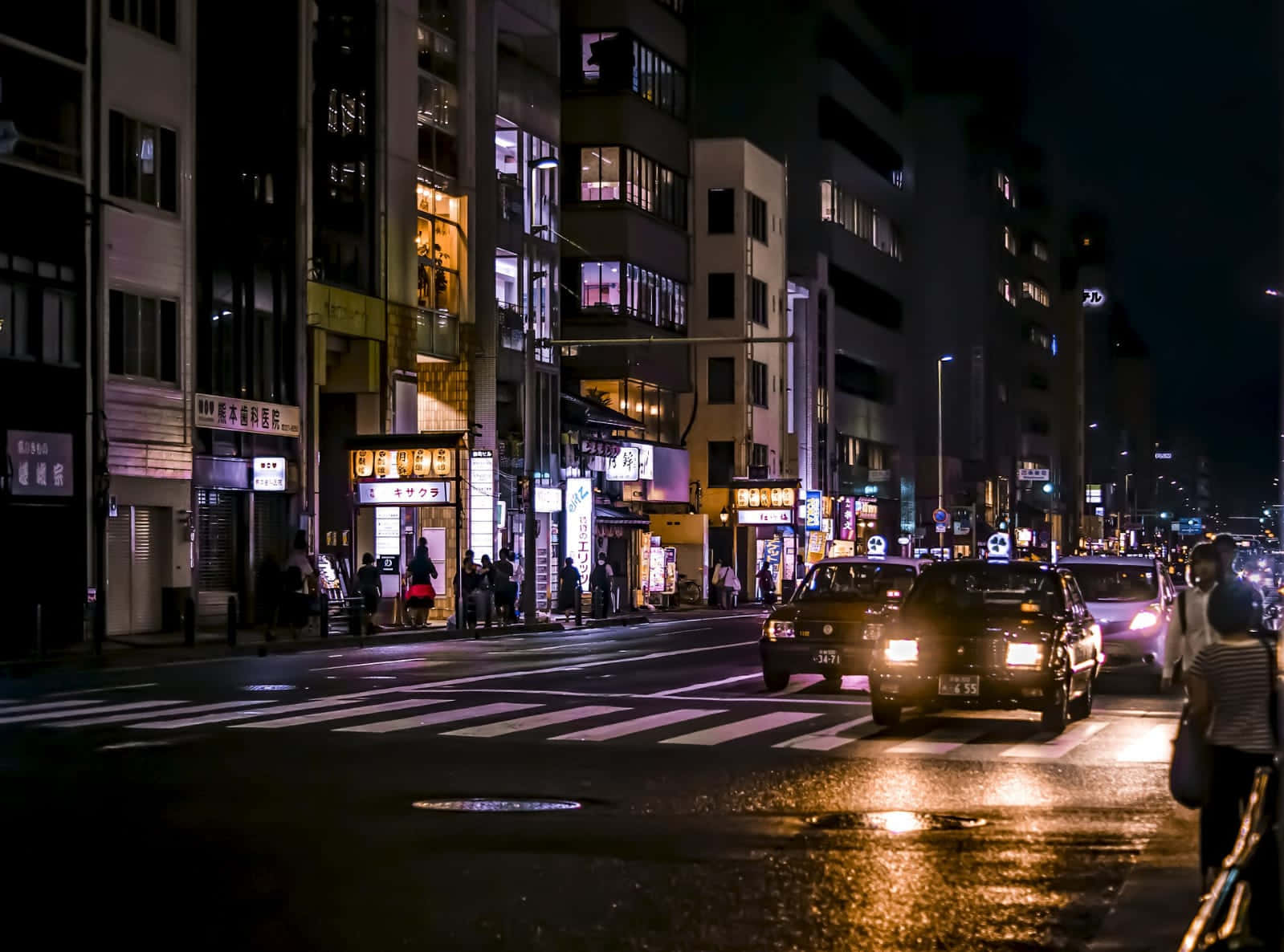 City Street 桌布 壁紙 — 一條濕漉漉的城市街道在夜晚被發光的霓虹燈招牌和汽車頭燈照亮，反射在雨水濕滑的路面上。