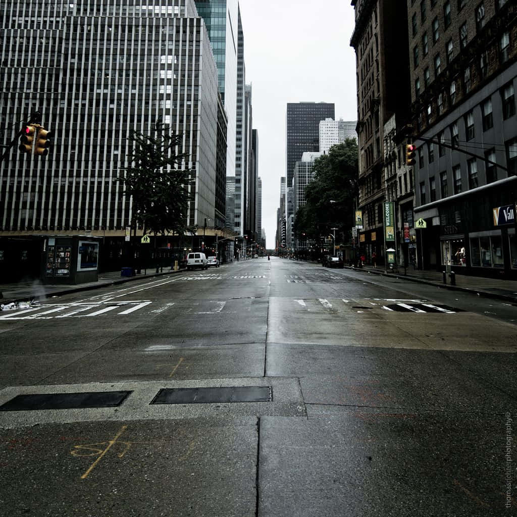 City Street 桌布 壁紙 — 一條濕漉漉的城市街道在陰天的高聳摩天大樓之間延伸，微弱的交通燈閃爍著。