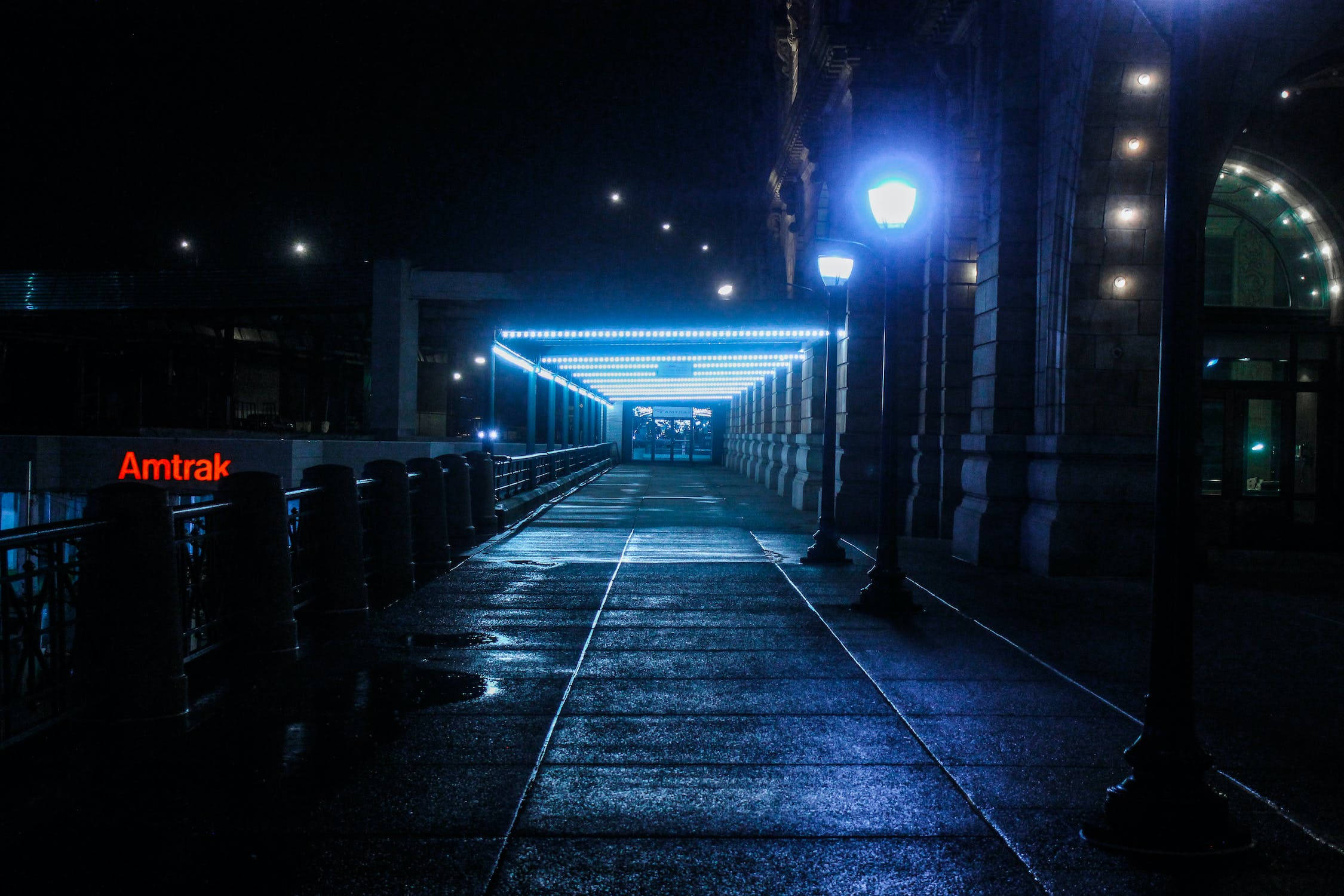 城市 桌布 壁紙 — 一條濕漉漉的夜間步道，在發光的藍色燈光下，通往Amtrak車站入口。