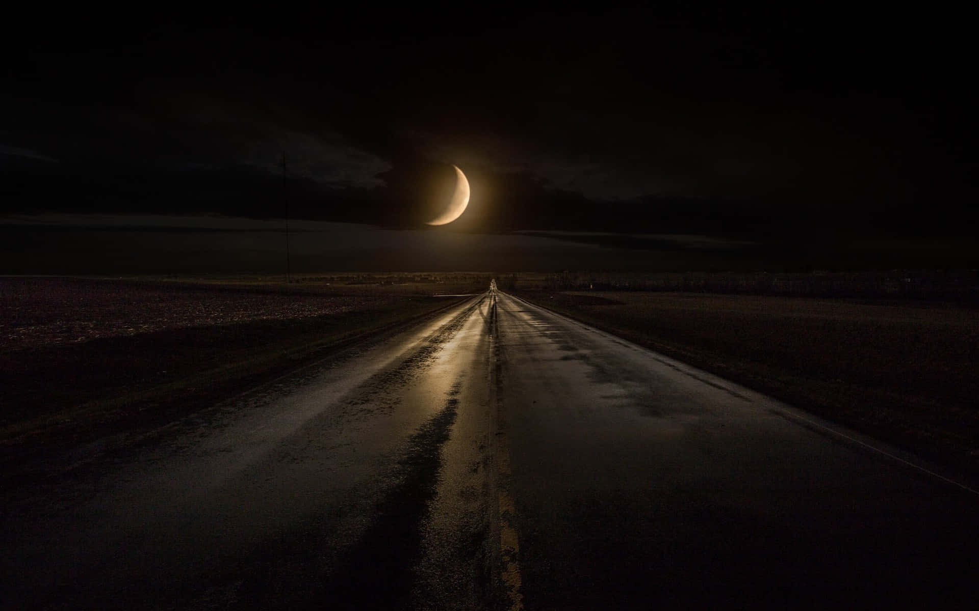 Midnight 桌布 壁紙 — 一條濕漉漉的道路在廣闊空曠的風景中，在發光的彎月下延伸進黑暗。