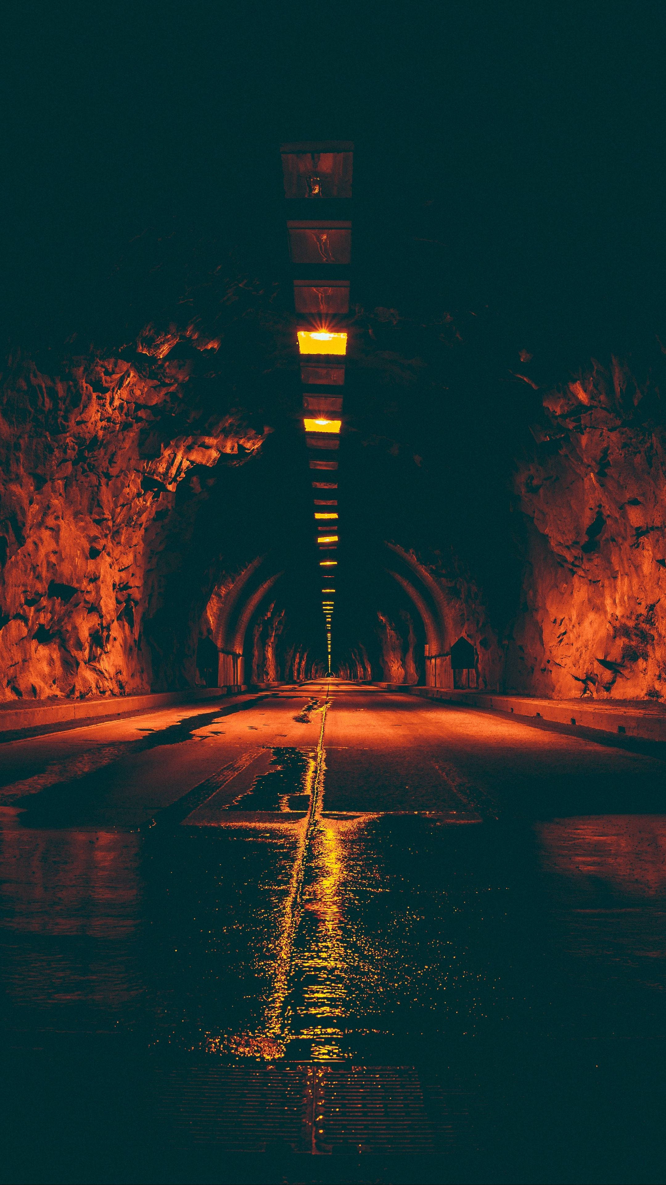 tunnel 桌布 壁紙 — 一條濕漉漉的道路在黑暗的隧道內，被溫暖的橙色燈光照亮，倒映在水面上。