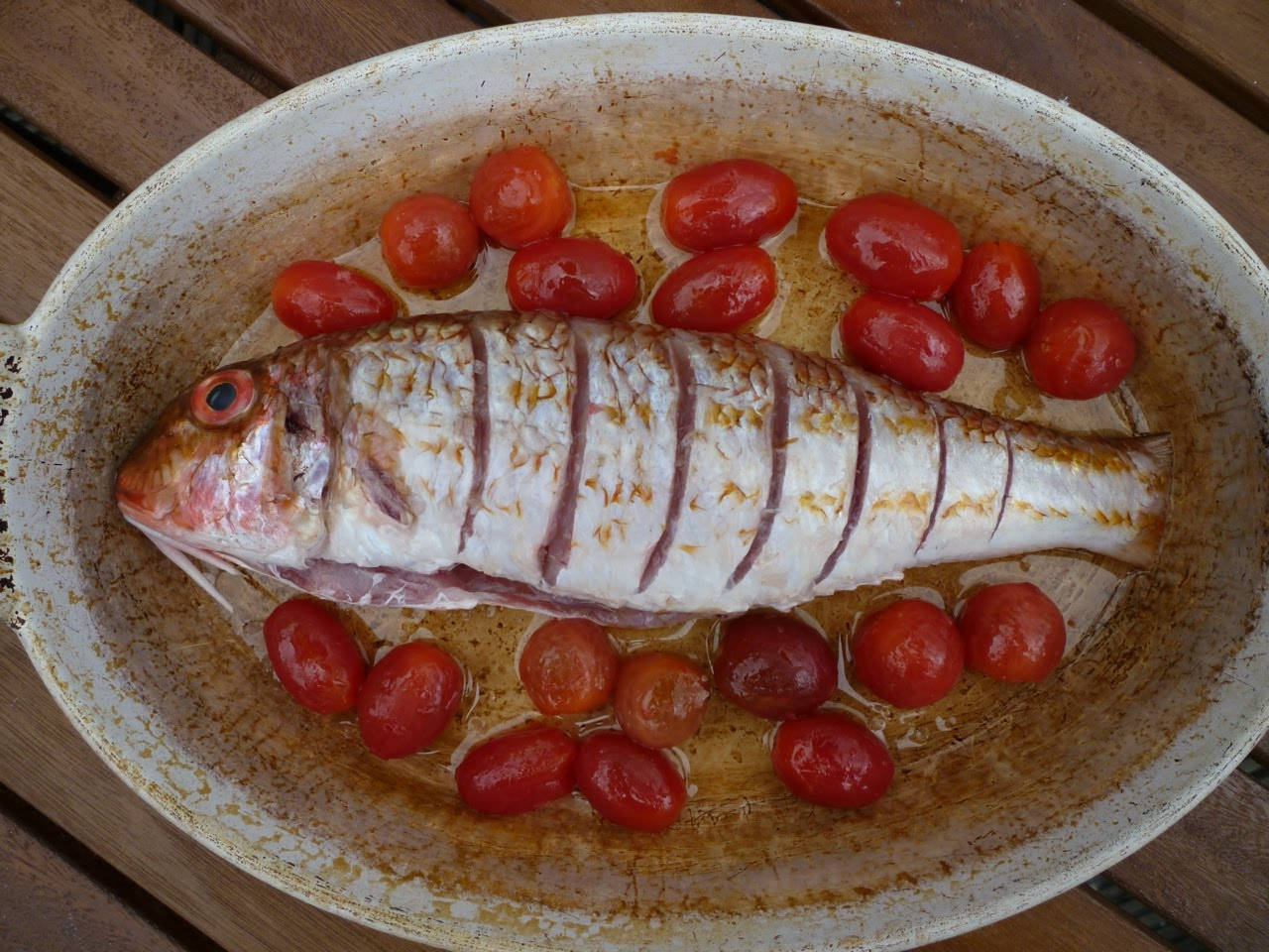 dishes 桌布 壁紙 — 一條烤全魚，魚皮劃開，搭配小番茄，放在木桌上的質樸烤盤中。