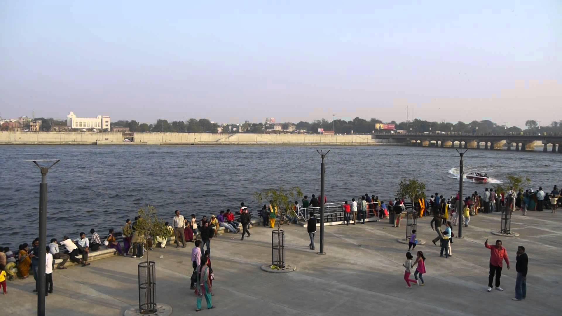 Ahmedabad 桌布 壁紙 — 一條熙熙攘攘的河濱長廊，人們在朦朧的天空下享受水邊的樂趣。