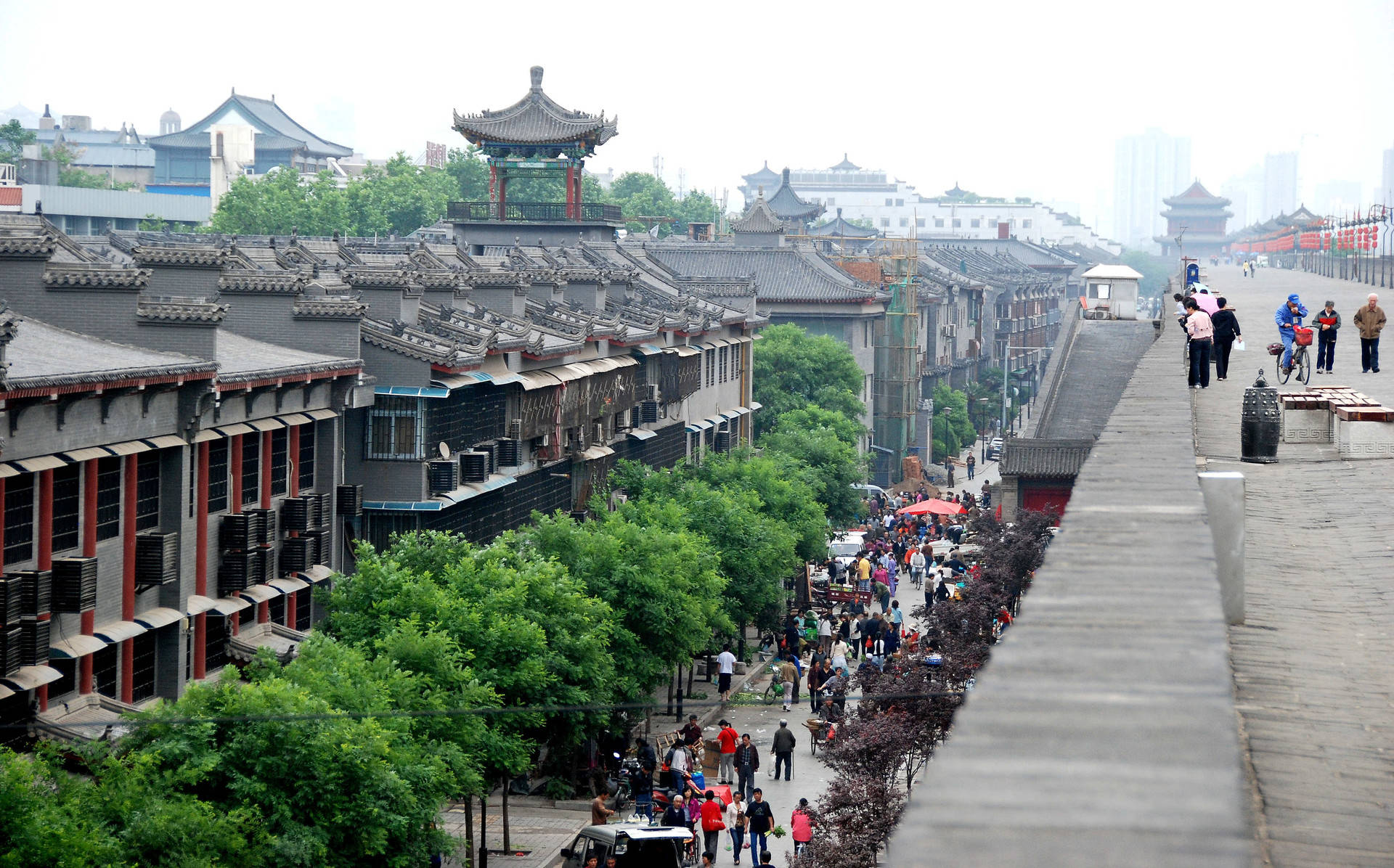 Xian 桌布 壁紙 — 一條熱鬧的傳統中國街道，有瓦片屋頂、綠樹，以及行人在陰天沿著石坡行走。