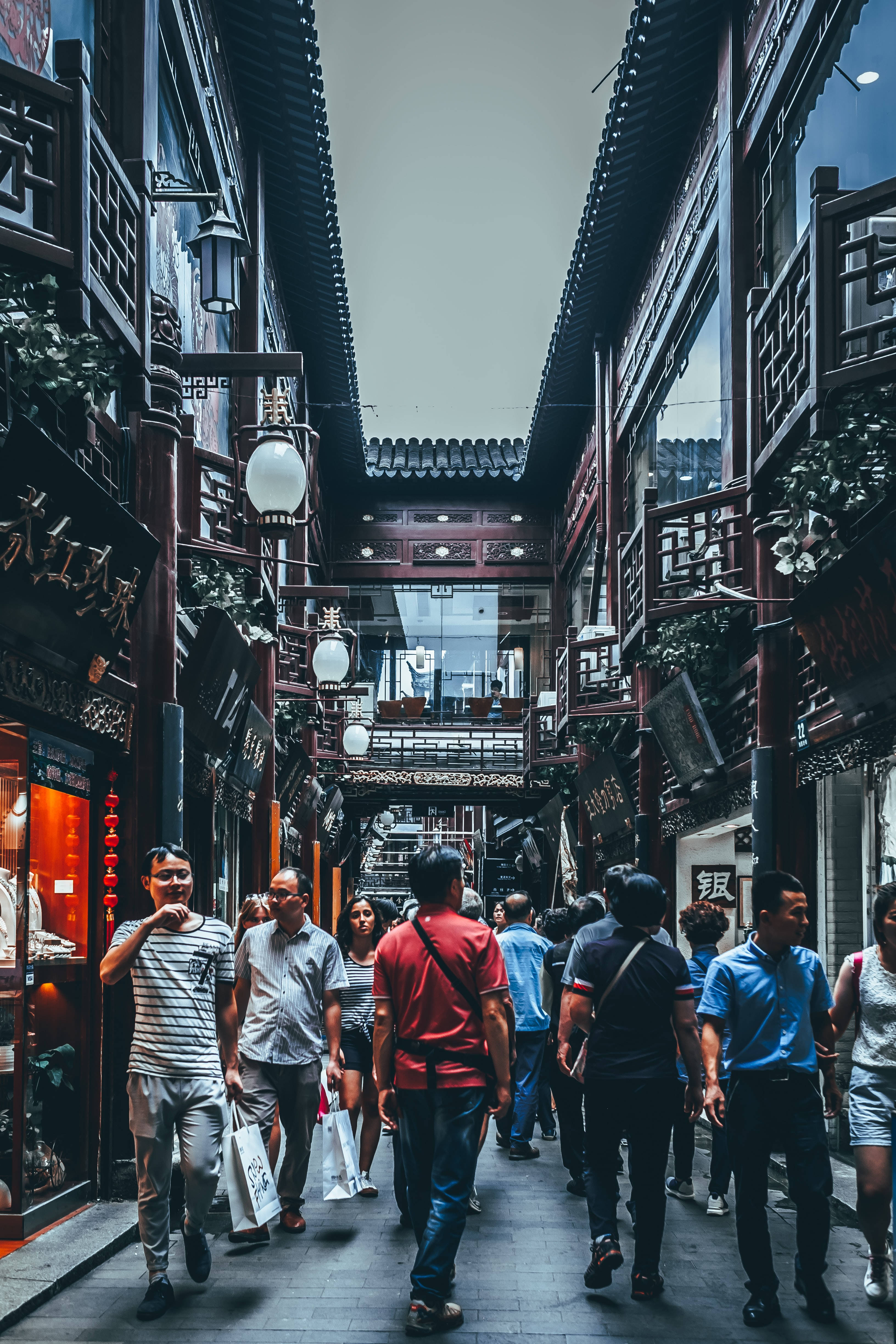 人物 桌布 壁紙 — 一條熱鬧的狹窄小巷，兩旁是傳統中式建築，行人走在華麗的木製陽台下。
