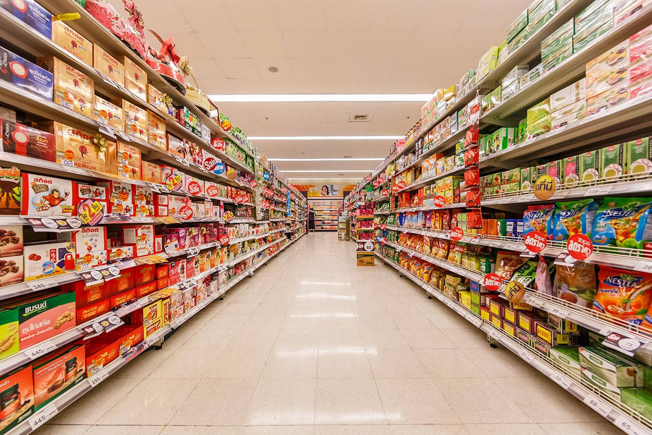 Shopping 桌布 壁紙 — 一條燈光明亮的超市通道，擺滿了色彩繽紛的包裝零食和穀物，一直延伸到遠方。