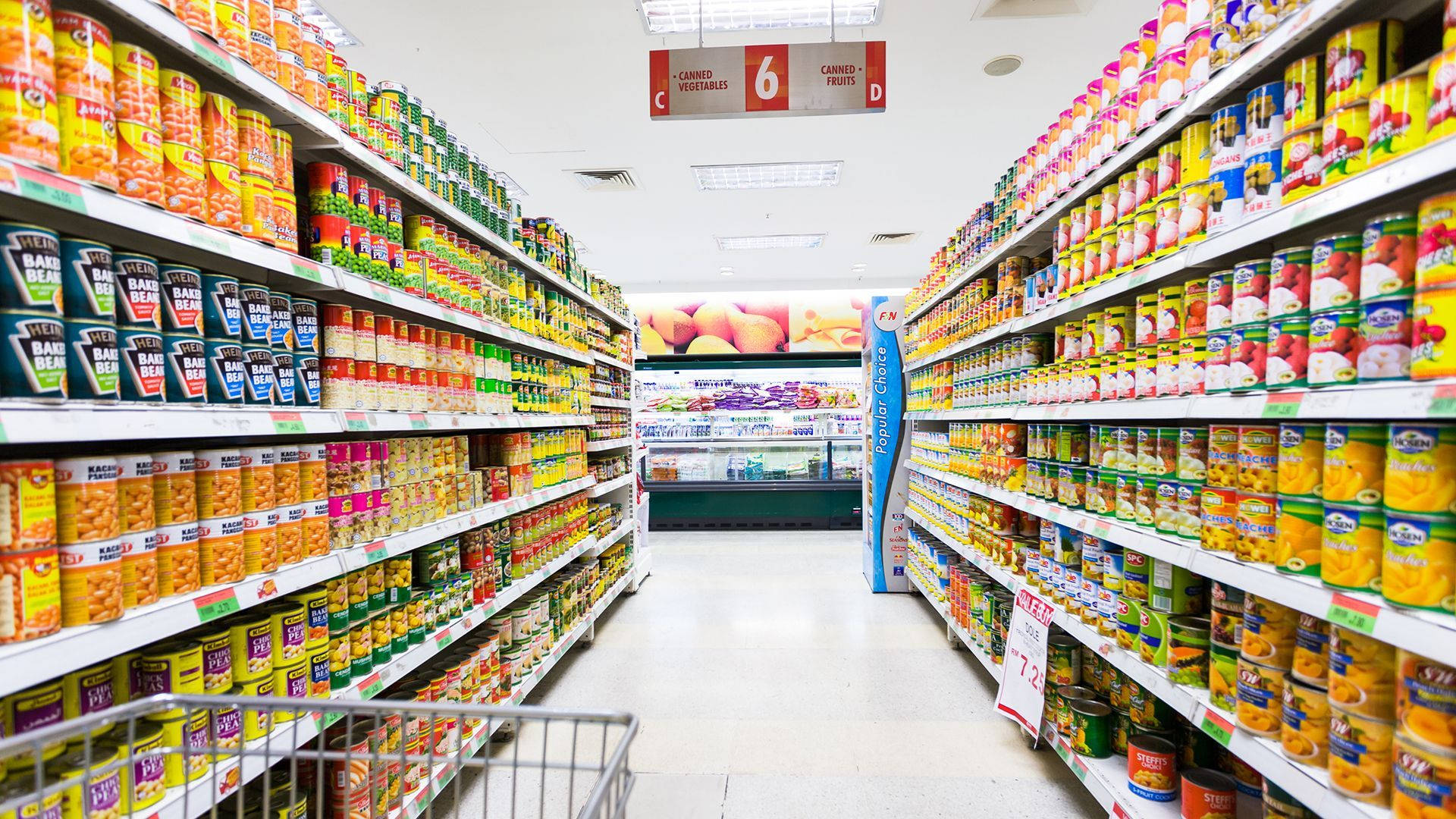 Shopping 桌布 壁紙 — 一條燈光明亮的超市通道，擺滿色彩繽紛的罐頭食品，一直延伸到遠方。