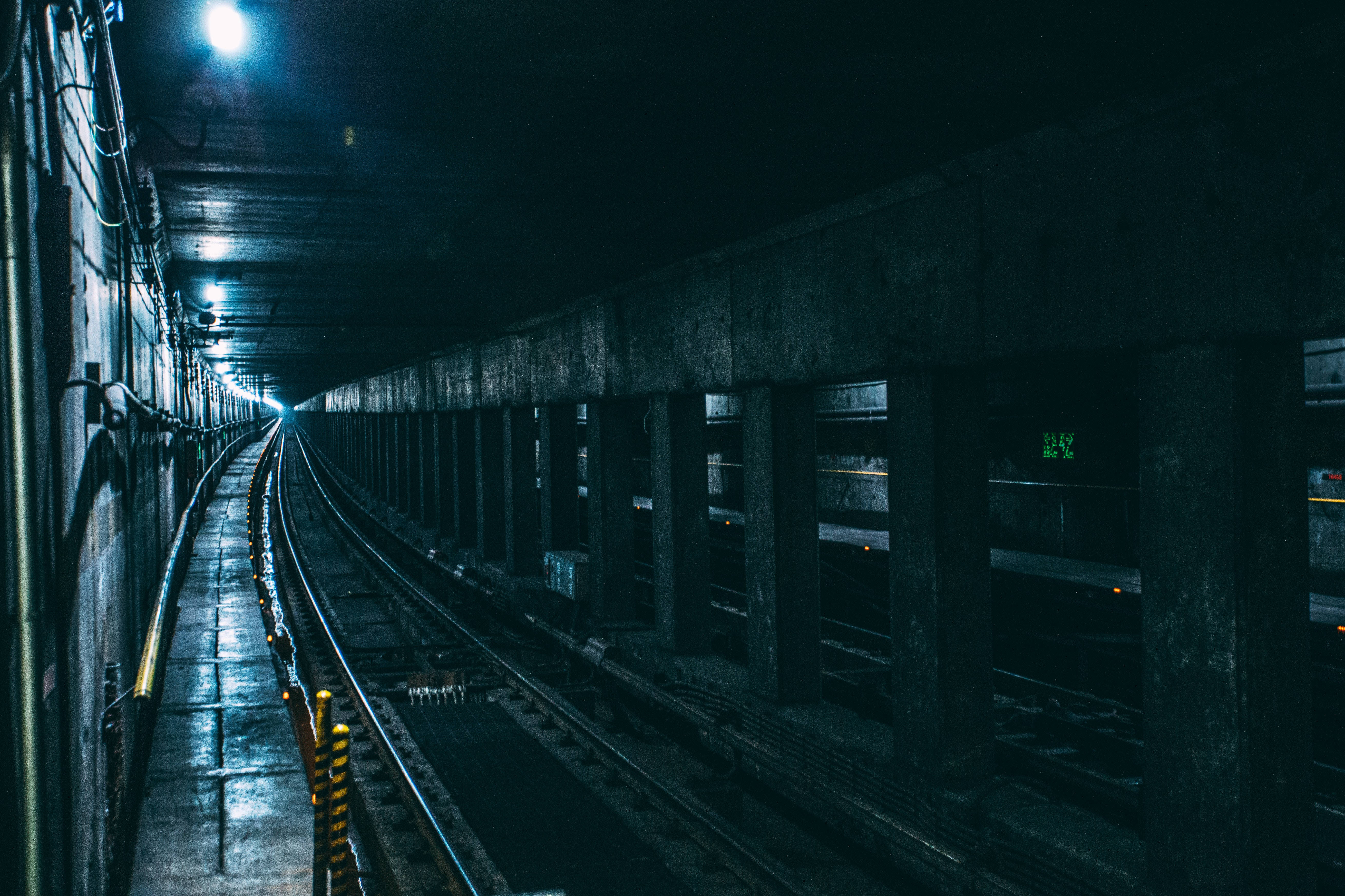 Subway 桌布 壁紙 — 一條燈光昏暗的地鐵隧道，潮濕的軌道在單一頭頂燈光下延伸至黑暗之中。