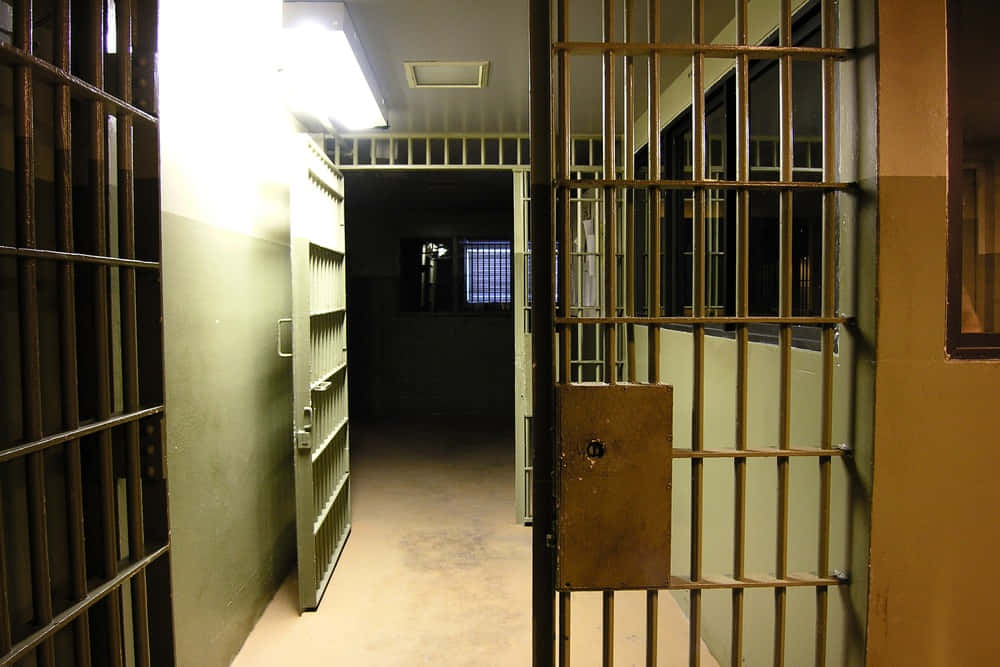 Prison 桌布 壁紙 — 一條燈光昏暗的監獄走廊，設有金屬鐵欄門，頭頂上的螢光燈閃爍不定。