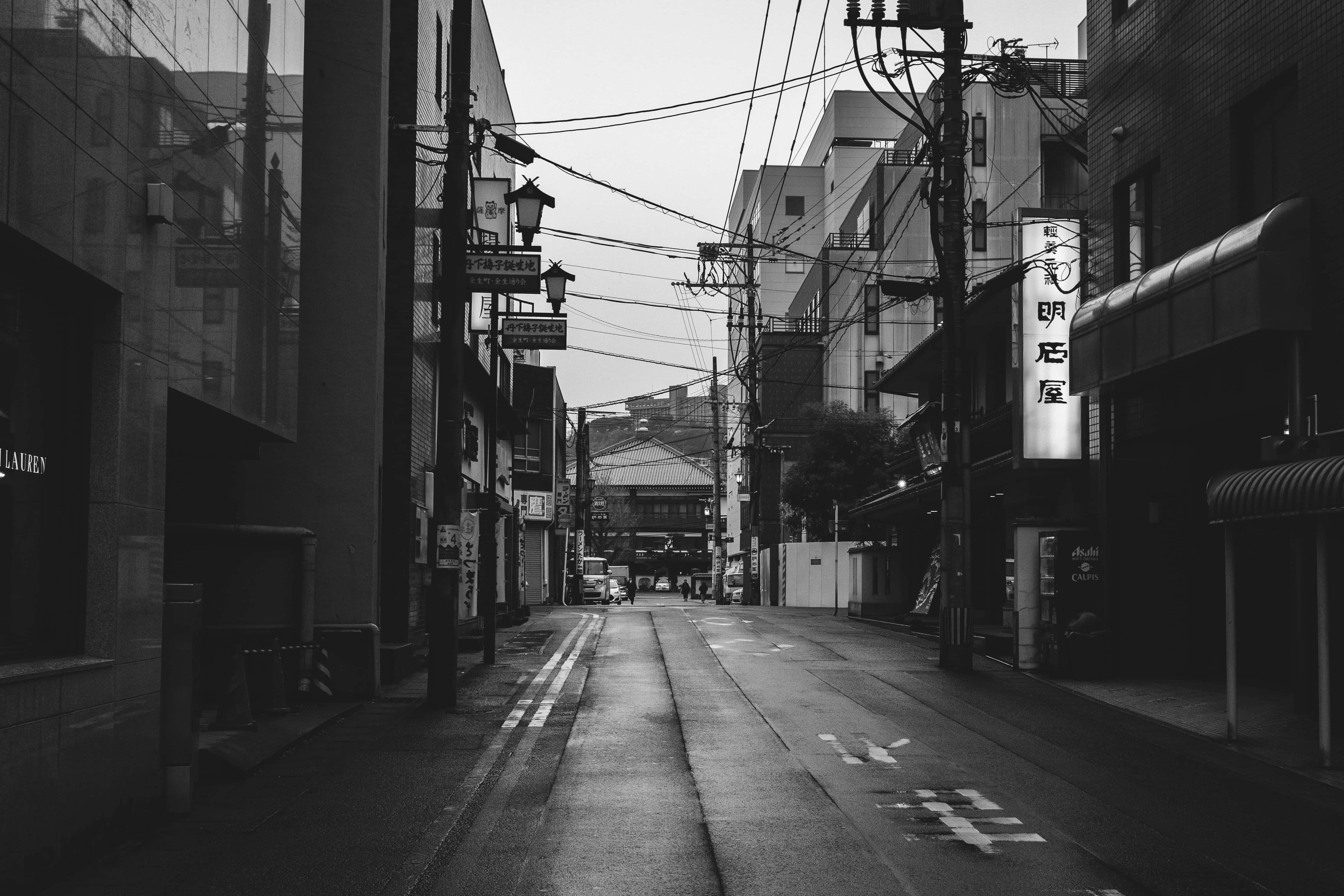 Aesthetic Black And White 桌布 壁紙 — 一條狹窄城市小巷的黑白景觀，濕漉漉的路面反射出高樓之間架空電線和發光招牌的倒影。