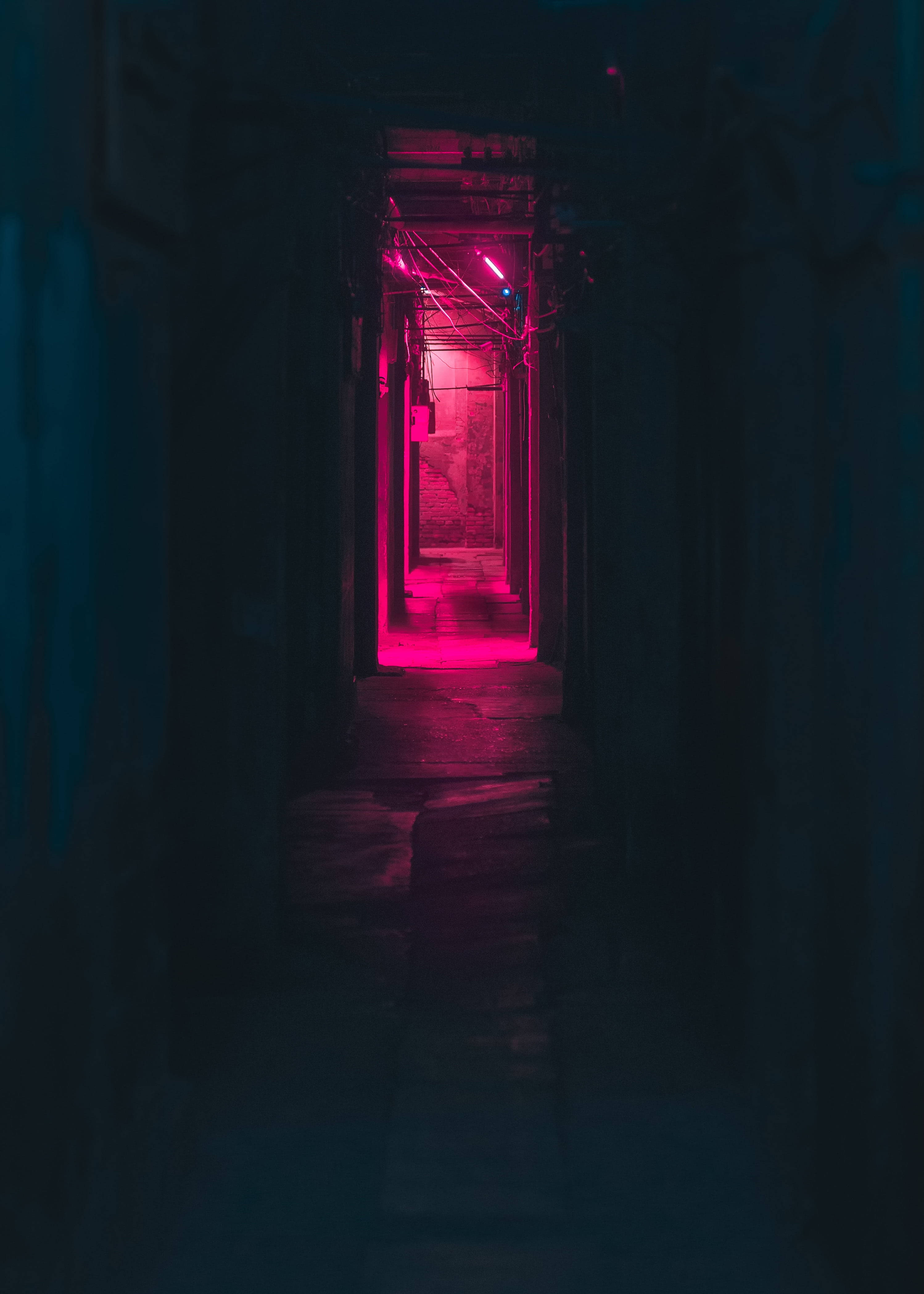 Dark Neon 桌布 壁紙 — 一條狹窄昏暗的小巷，盡頭被強烈的粉紅色霓虹燈照亮，營造出陰鬱的城市隧道效果。