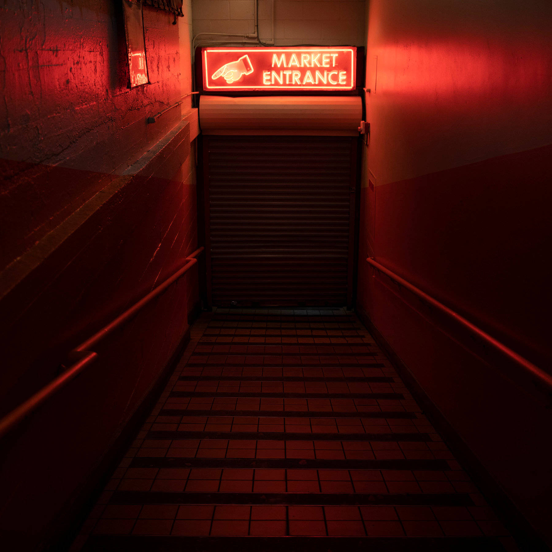 Pike Place Market 桌布 壁紙 — 一條狹窄昏暗的走廊，被關閉的金屬門上方發光的「MARKET ENTRANCE」標誌的紅色霓虹燈照亮。