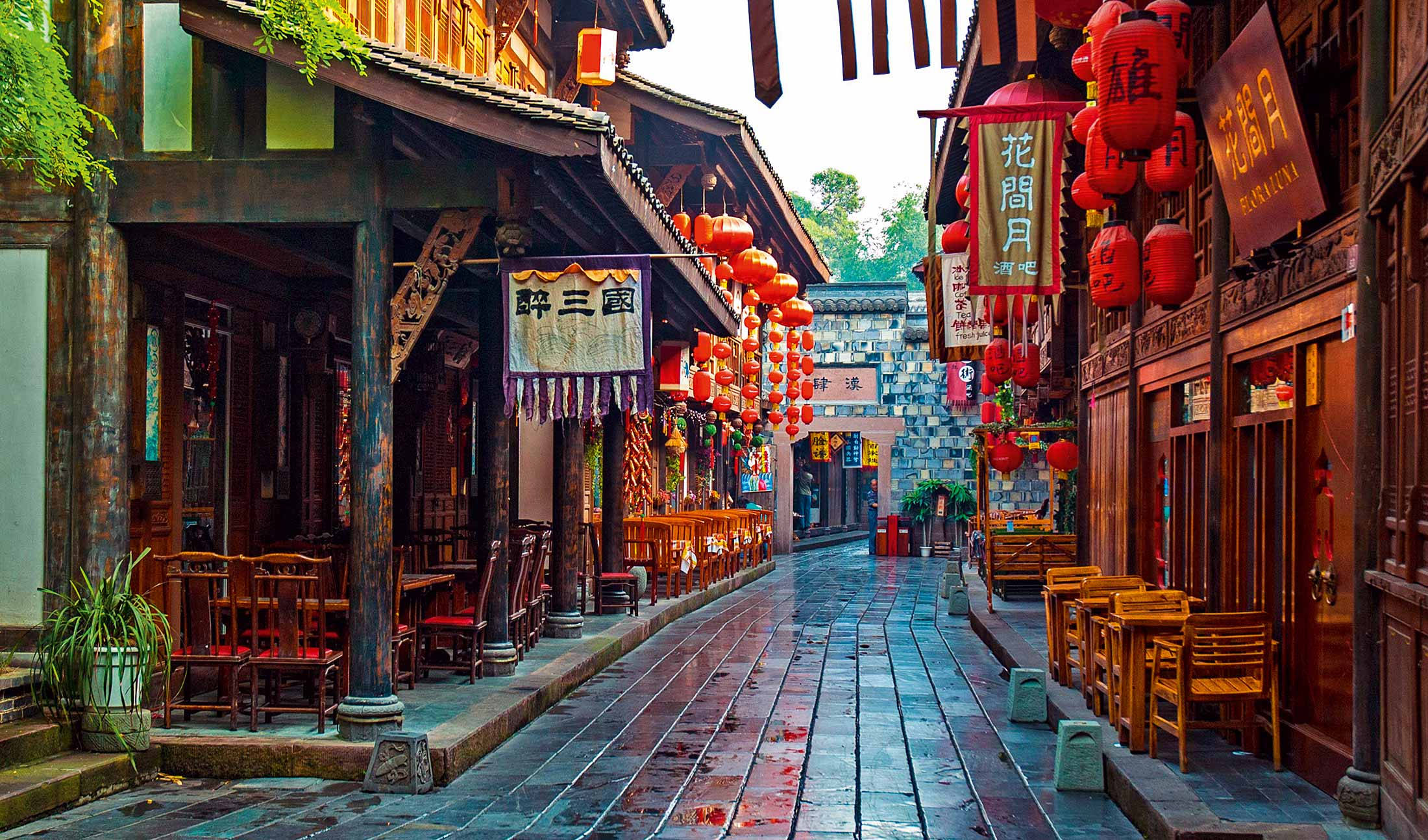 Chengdu 桌布 壁紙 — 一條狹窄潮濕的石頭街道，兩旁是傳統木建築，裝飾著紅燈籠和懸掛的招牌。