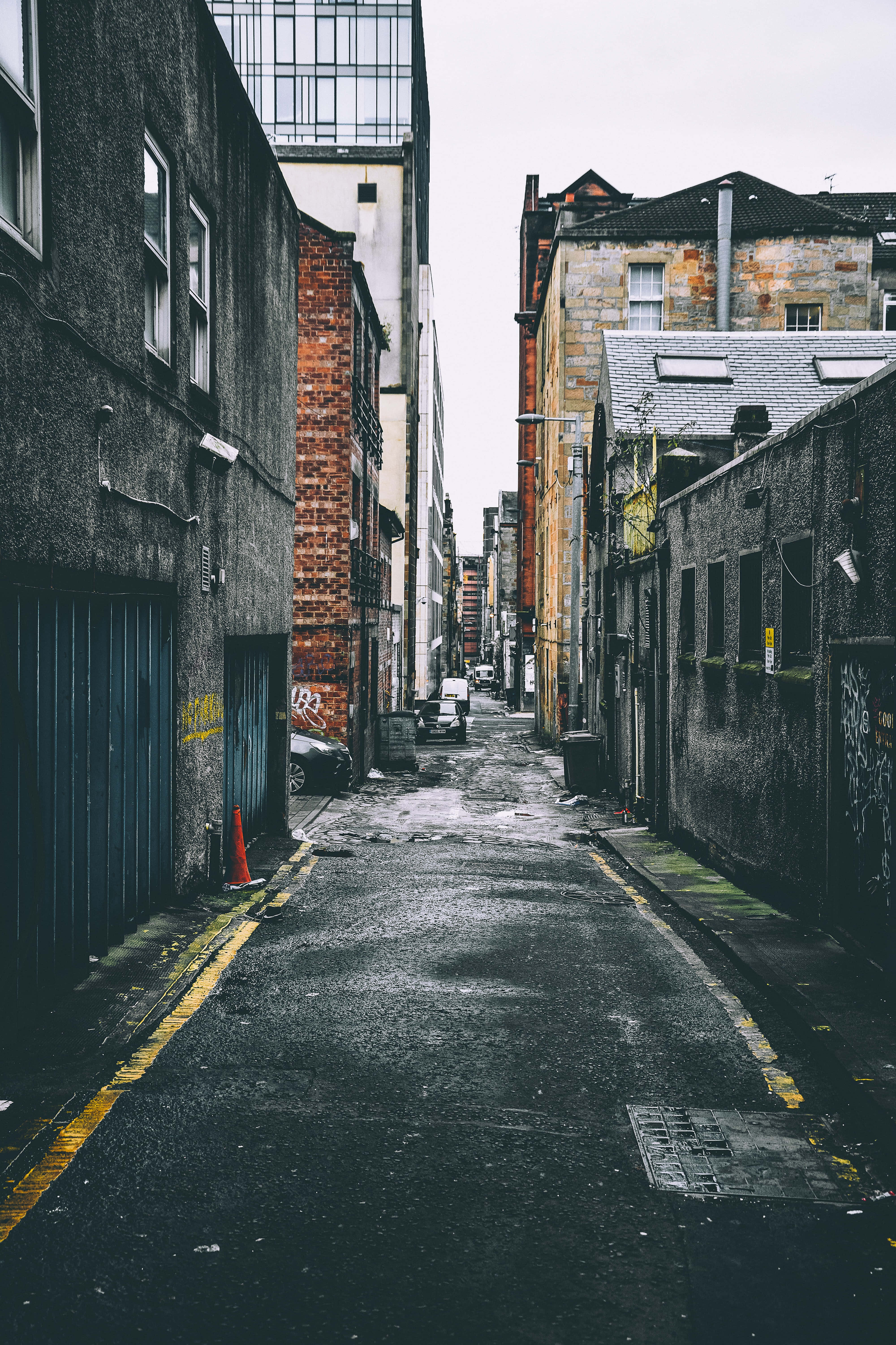 City Street 桌布 壁紙 — 一條狹窄的城市小巷，位於風化的磚和混凝土建築之間，天空多雲。