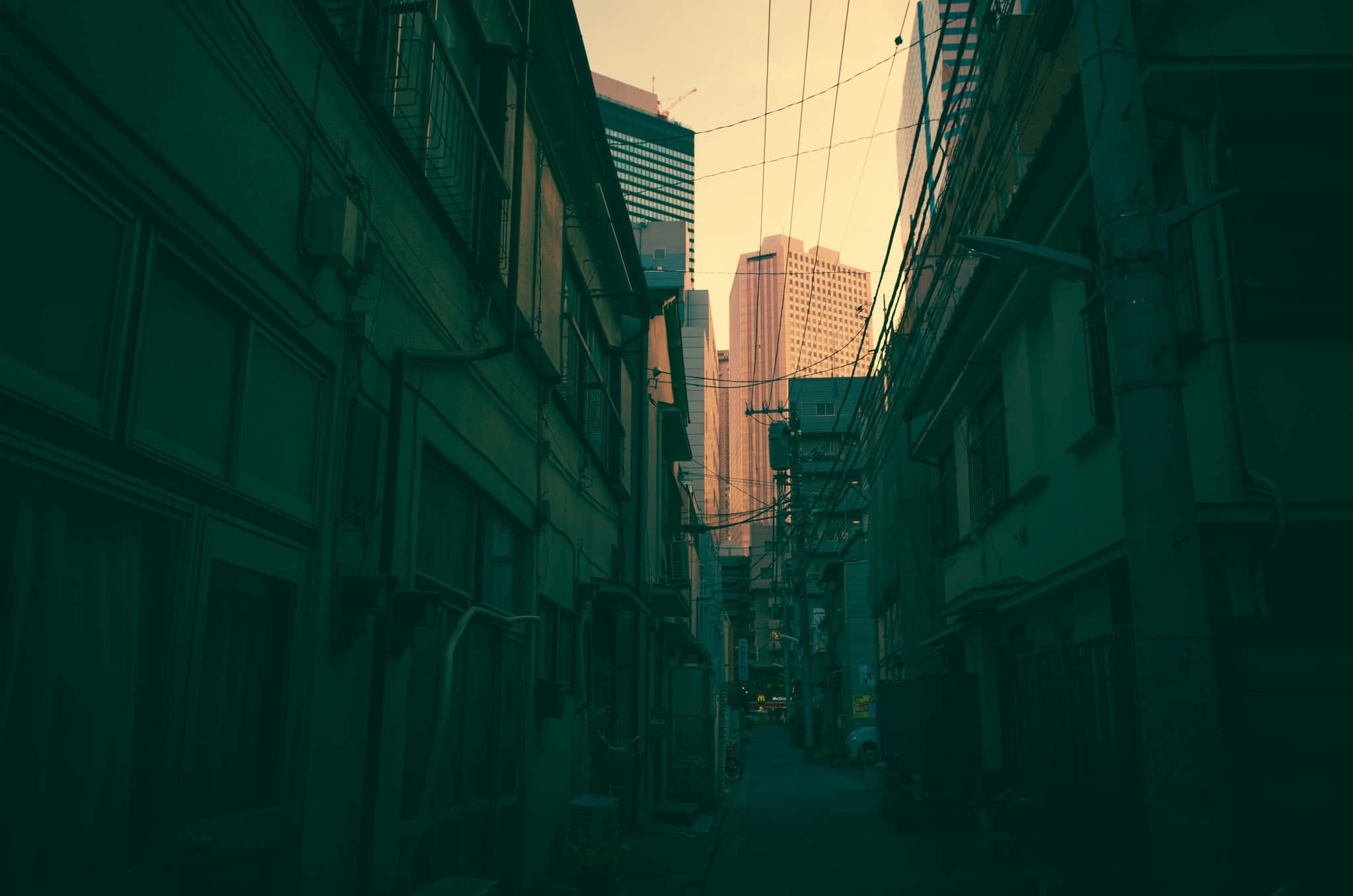 Dark Alleyway 桌布 壁紙 — 一條狹窄的城市小巷，兩旁是舊建築，纏繞的電線通向沐浴在溫暖夕陽餘暉中的高聳摩天大樓。