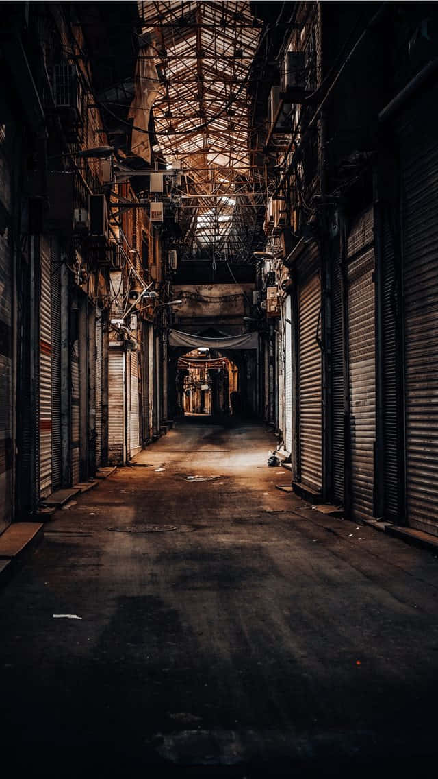 Alleyway 桌布 壁紙 — 一條狹窄的城市小巷，有關閉的金屬百葉窗和纏結的電線，在生鏽的金屬屋頂下沐浴在昏暗的金色光線中。