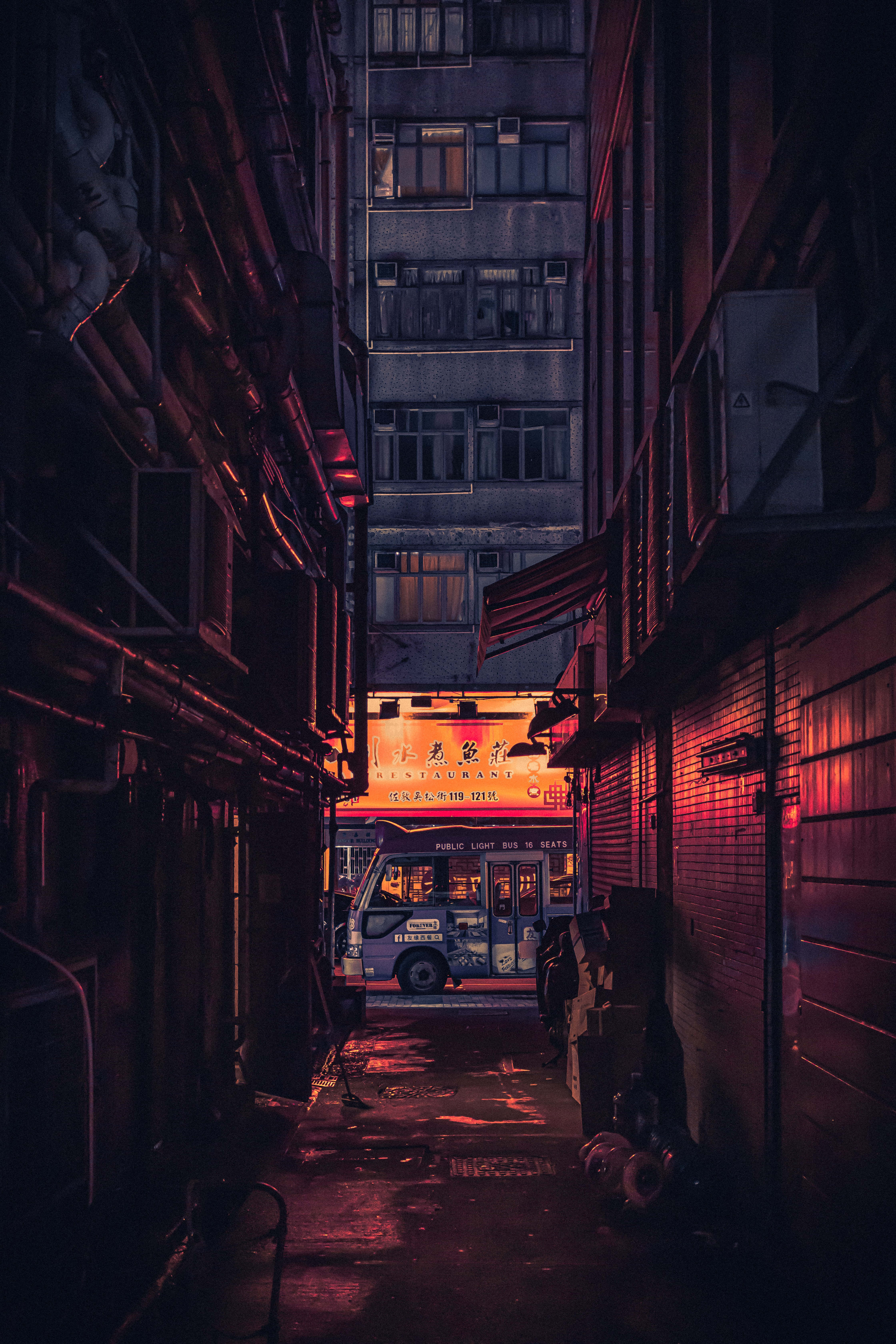 Alleyway 桌布 壁紙 — 一條狹窄的城市小巷，沐浴在深紅色的霓虹燈光中，一輛巴士停在盡頭髮光的招牌下。