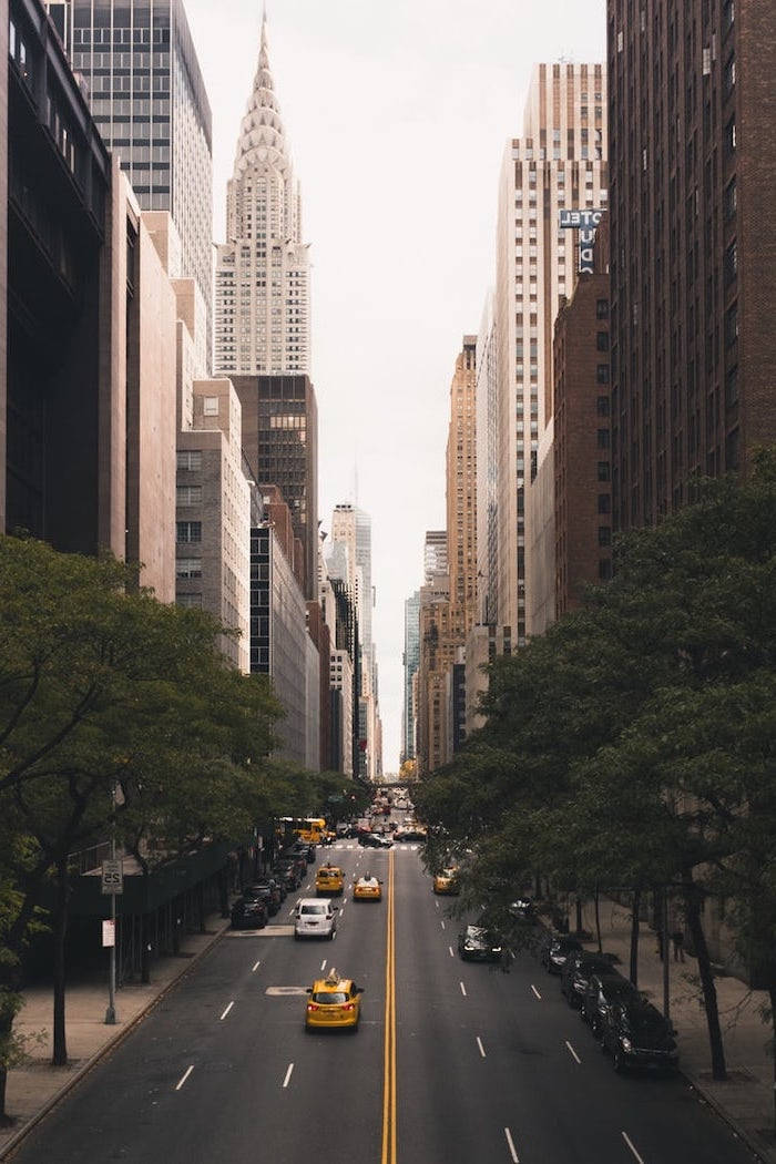 manhattan 桌布 壁紙 — 一條狹窄的城市街道，兩旁是高聳的摩天大樓，黃色的士駛向遠處標誌性的克萊斯勒大廈。