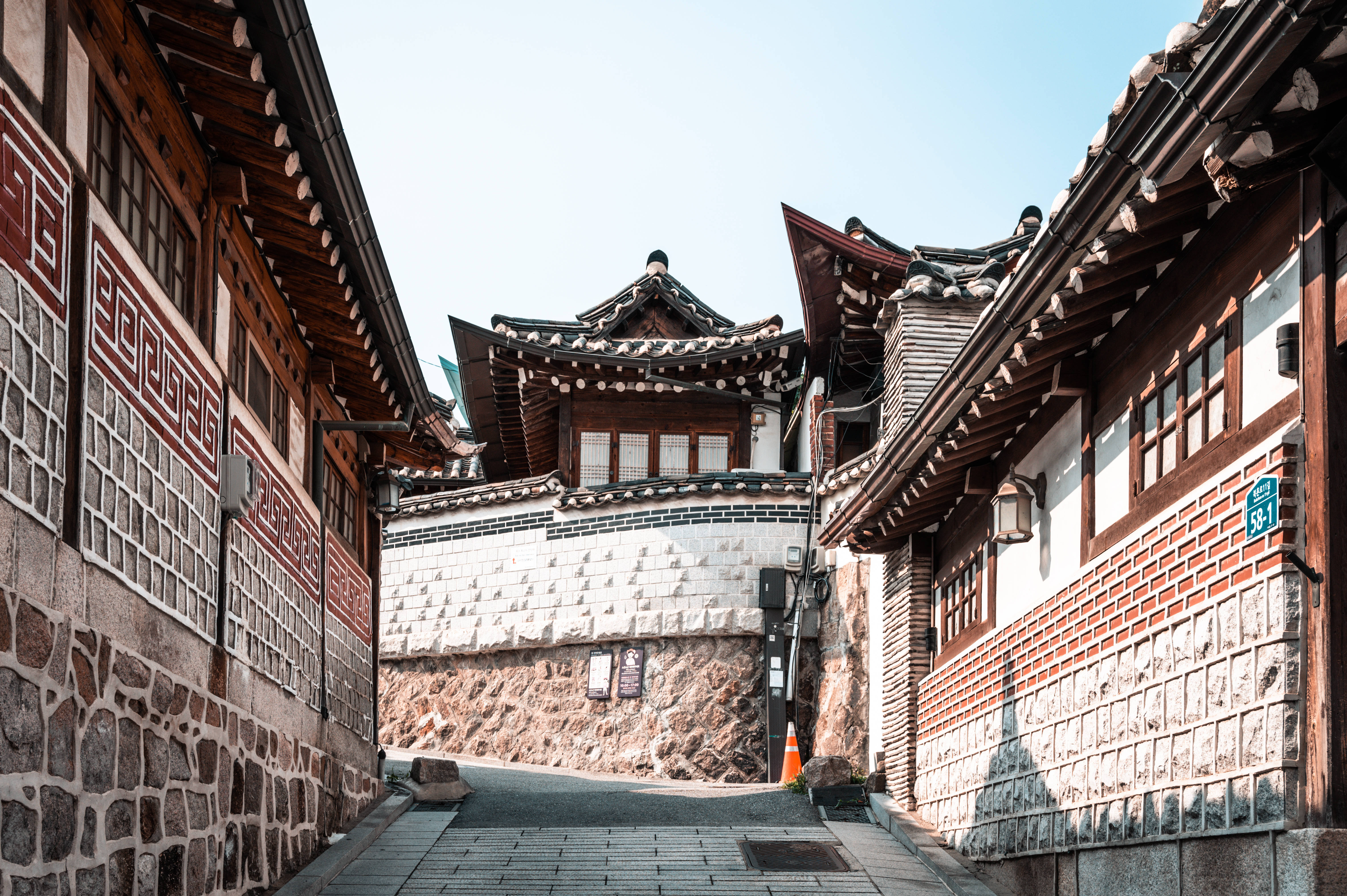 首爾 桌布 壁紙 — 一條狹窄的小巷，兩旁是傳統的韓國韓屋建築，在晴朗的藍天下。