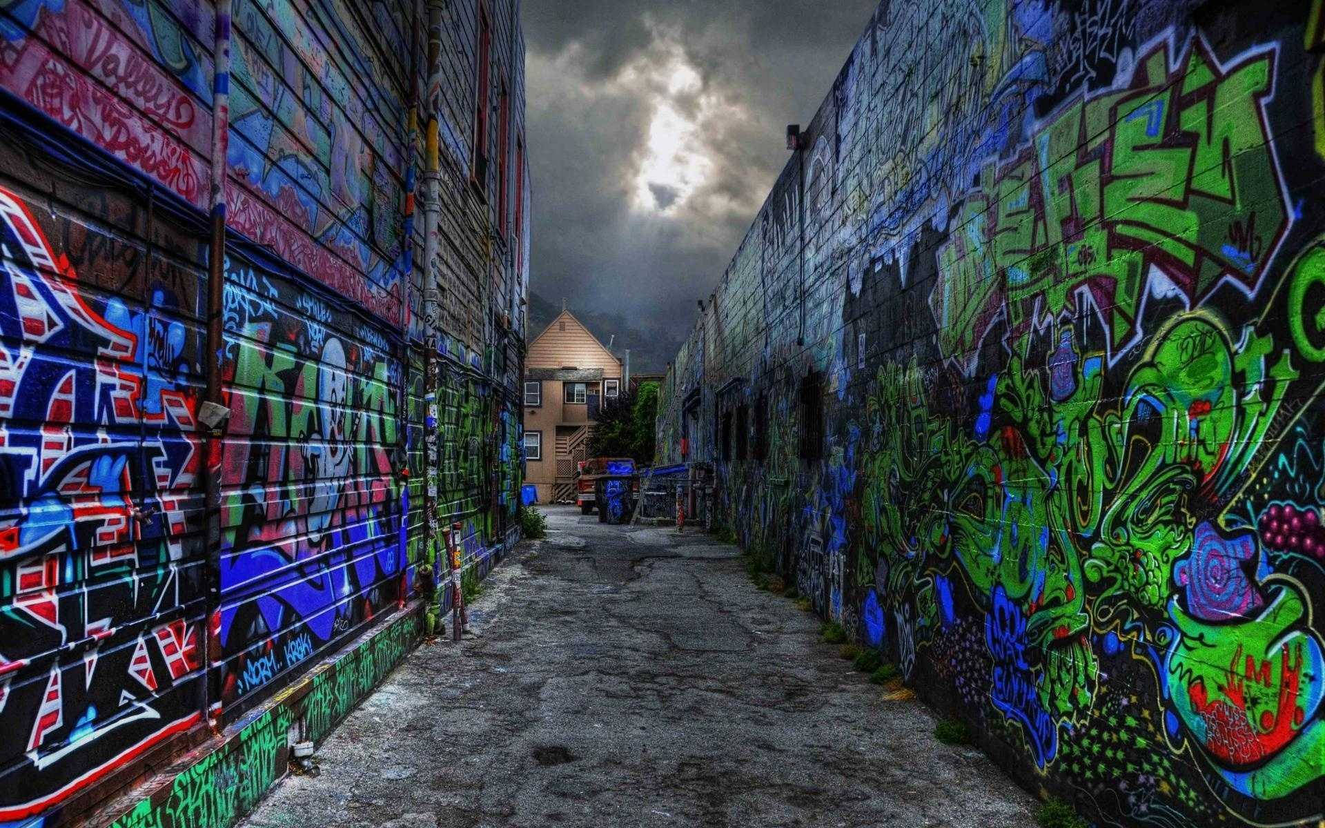 嘻哈 桌布 壁紙 — 一條狹窄的小巷，兩旁牆壁佈滿鮮豔的塗鴉，上方是戲劇性的多雲天空。