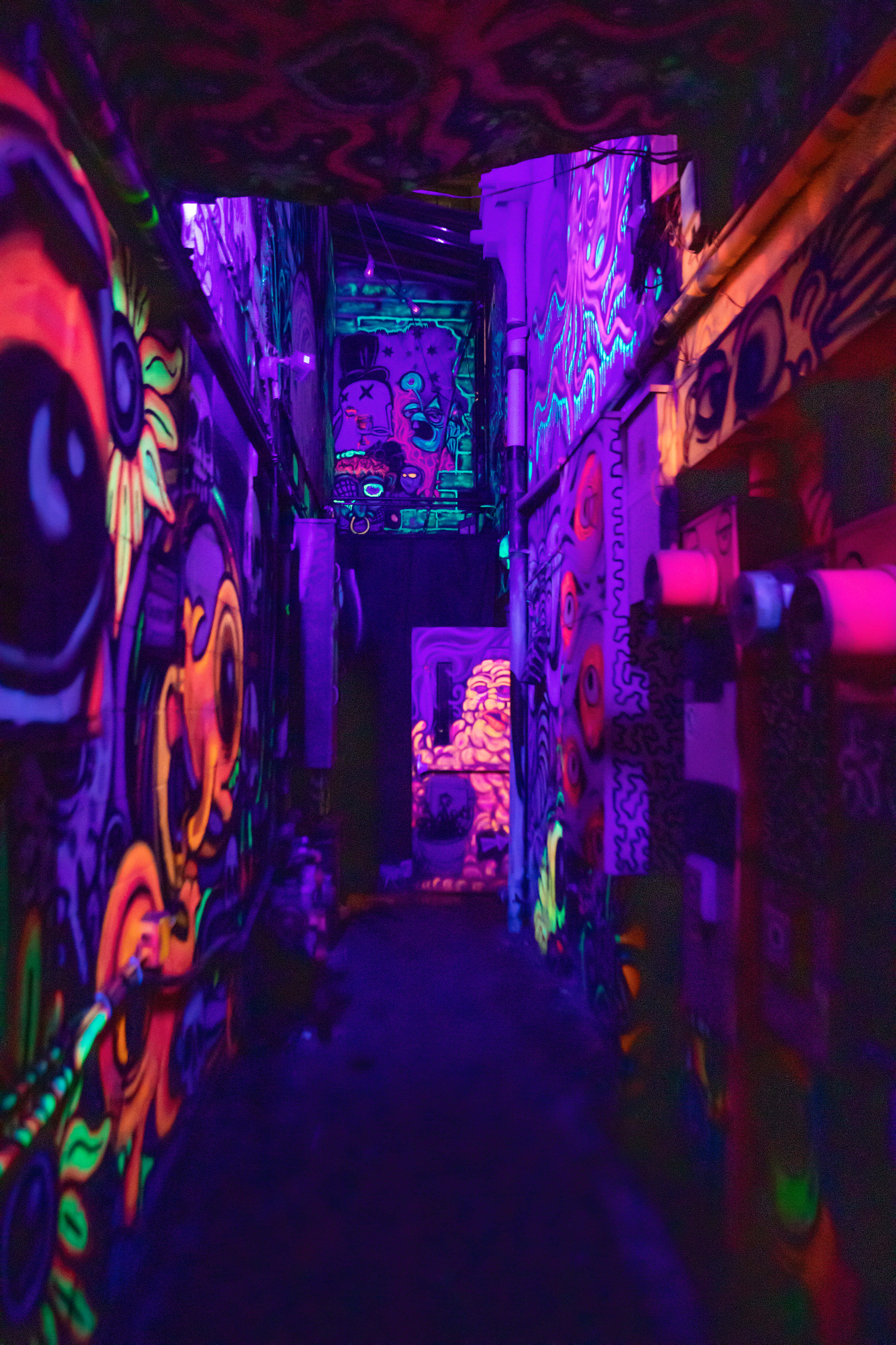 桌布 壁紙 — 一條狹窄的小巷，在黑光下散發著霓虹塗鴉的光芒，牆壁上覆蓋著充滿活力的迷幻藝術。
